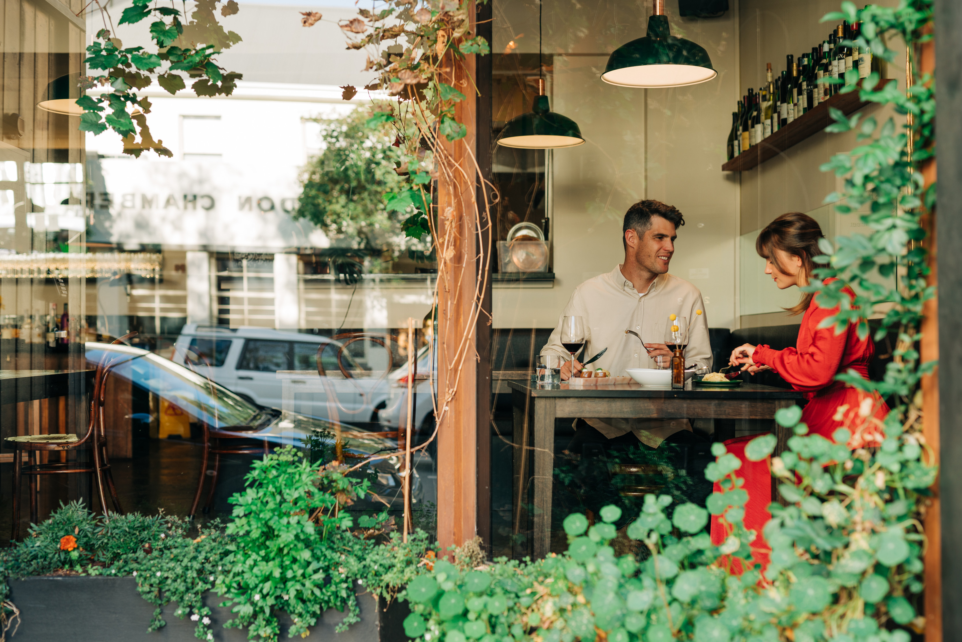 Image of a couple enjoying food through the window of the aesthetic Fico restaurant, surrounded by green plants.