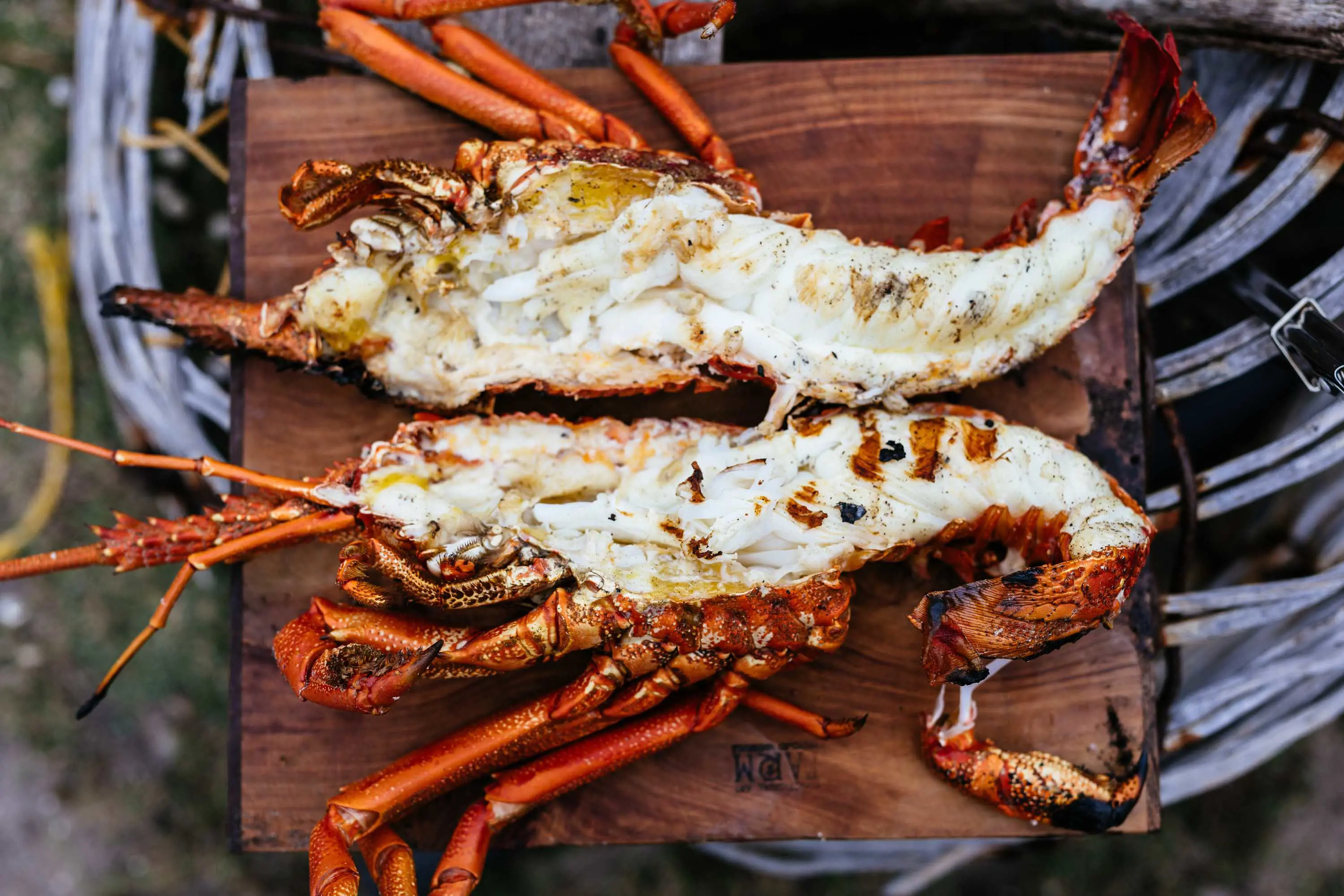 A large cooked crayfish, cut in half length-wise is displayed on a wooden board.  