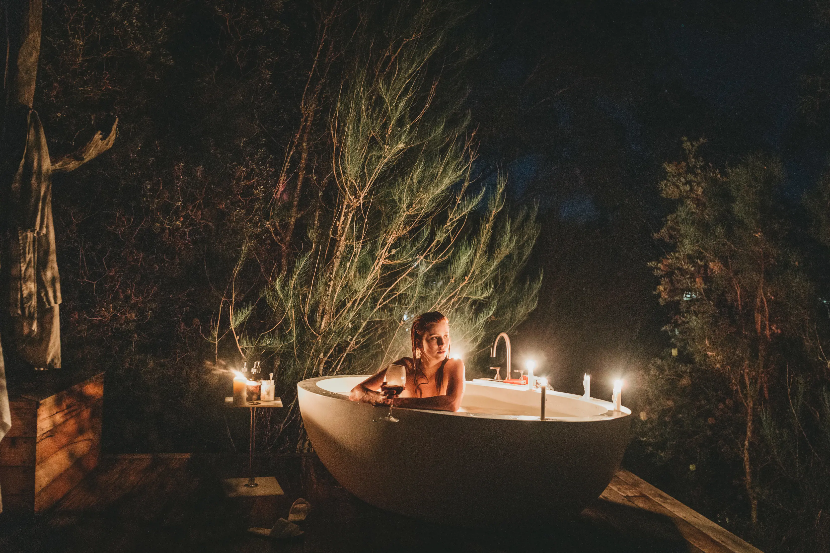 At night, a woman relaxes in a candle lit outdoor bathtub at The Retreat accomodation, Pumphouse Point.