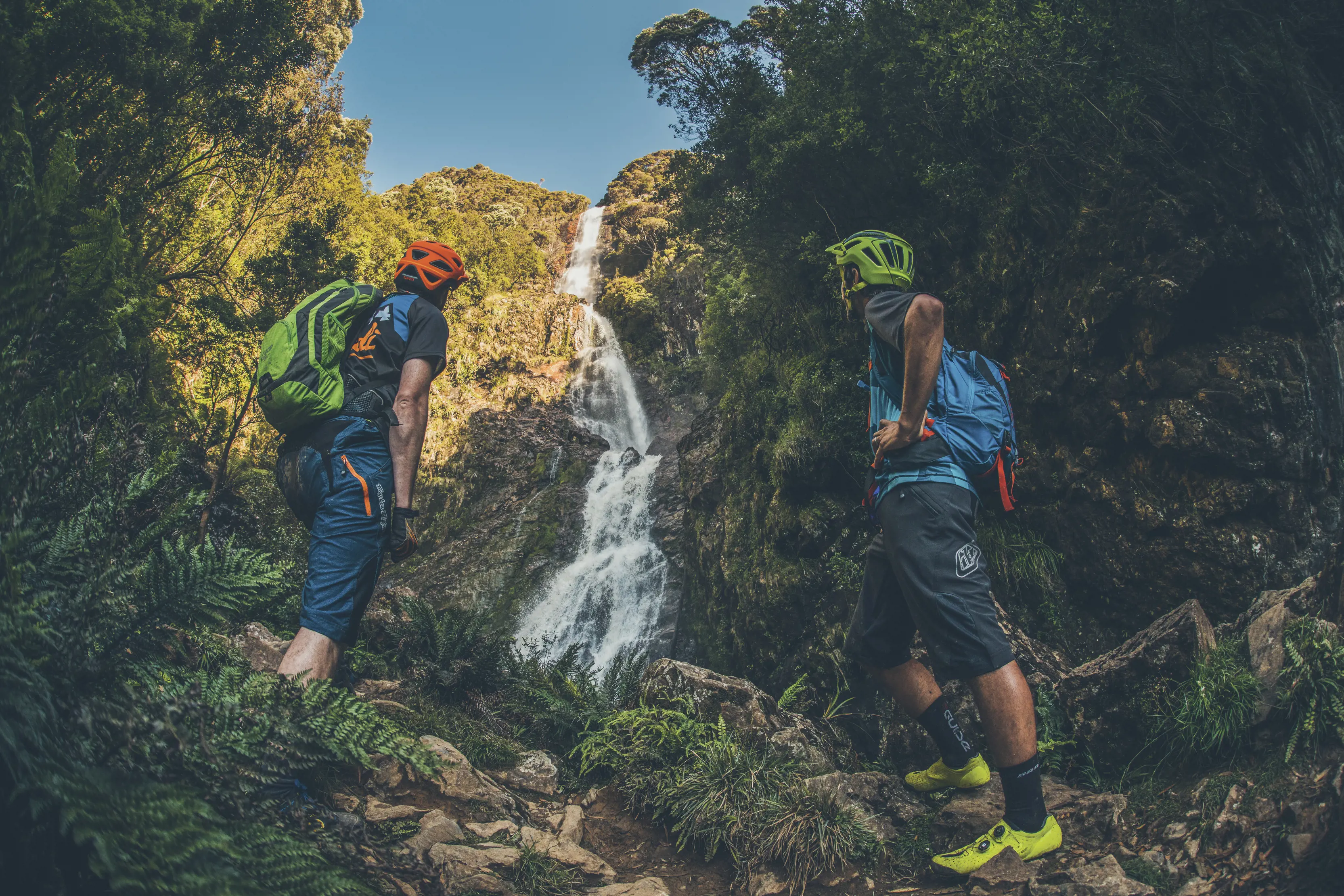 Two men in helmets at the foot of Montezuma Falls, stopping to look up at the waterfall.