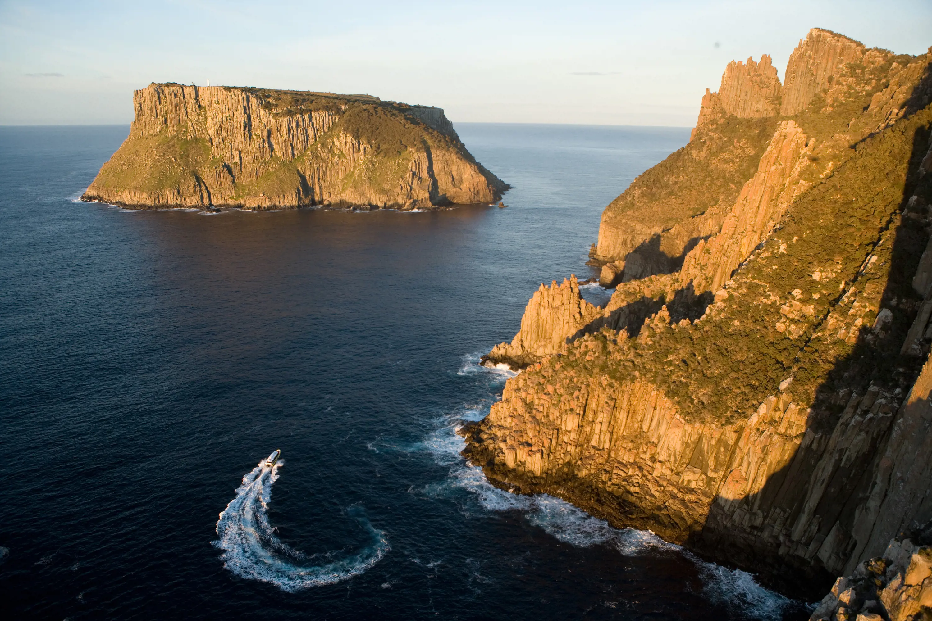 A aerial shot of a speed boat turning between Caper Pillar and Tasman Island, Tasmania