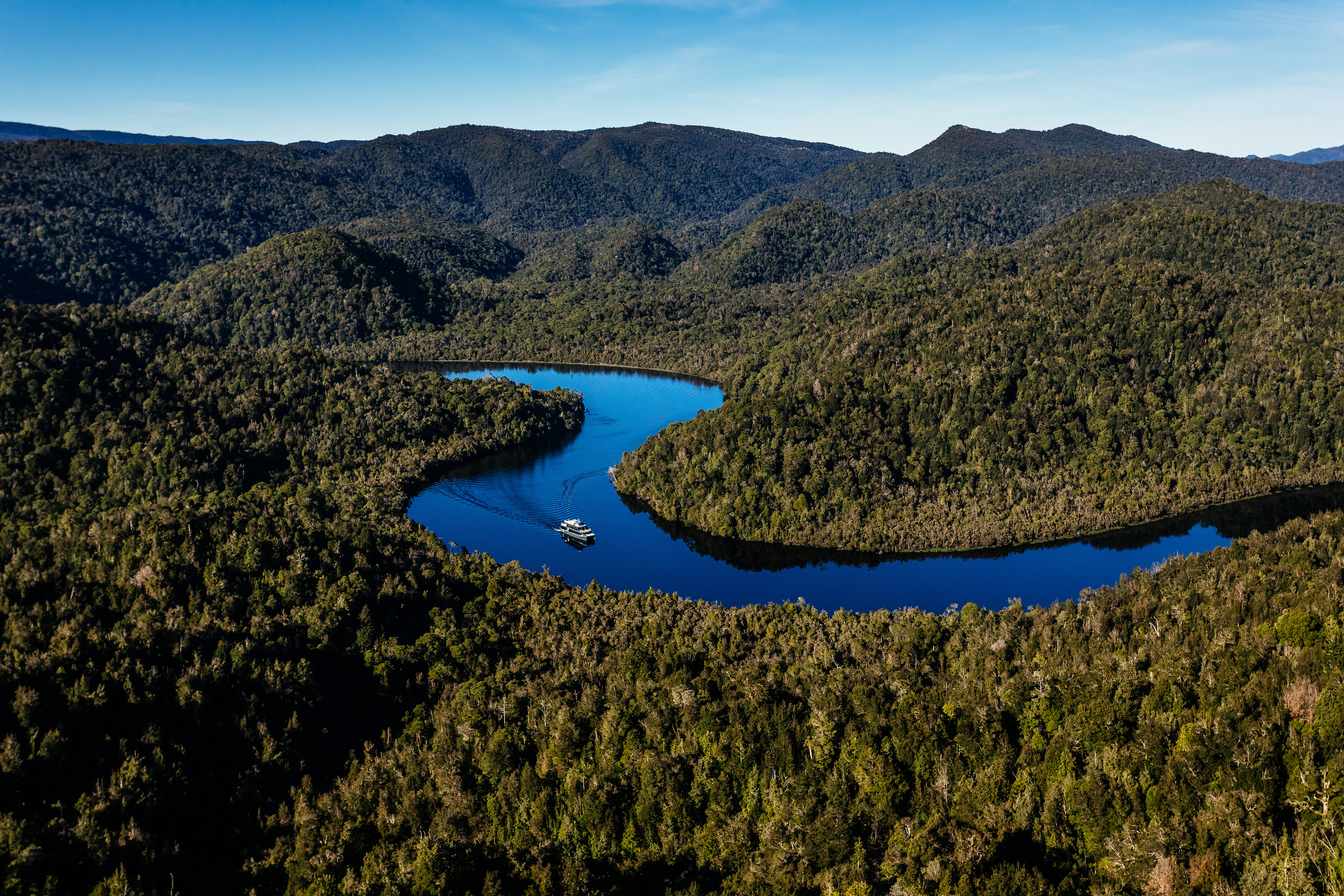 Incredible aerial image of Gordon River Cruises, piloting through Gordon River, surrounded by lush forest on either side of the river.