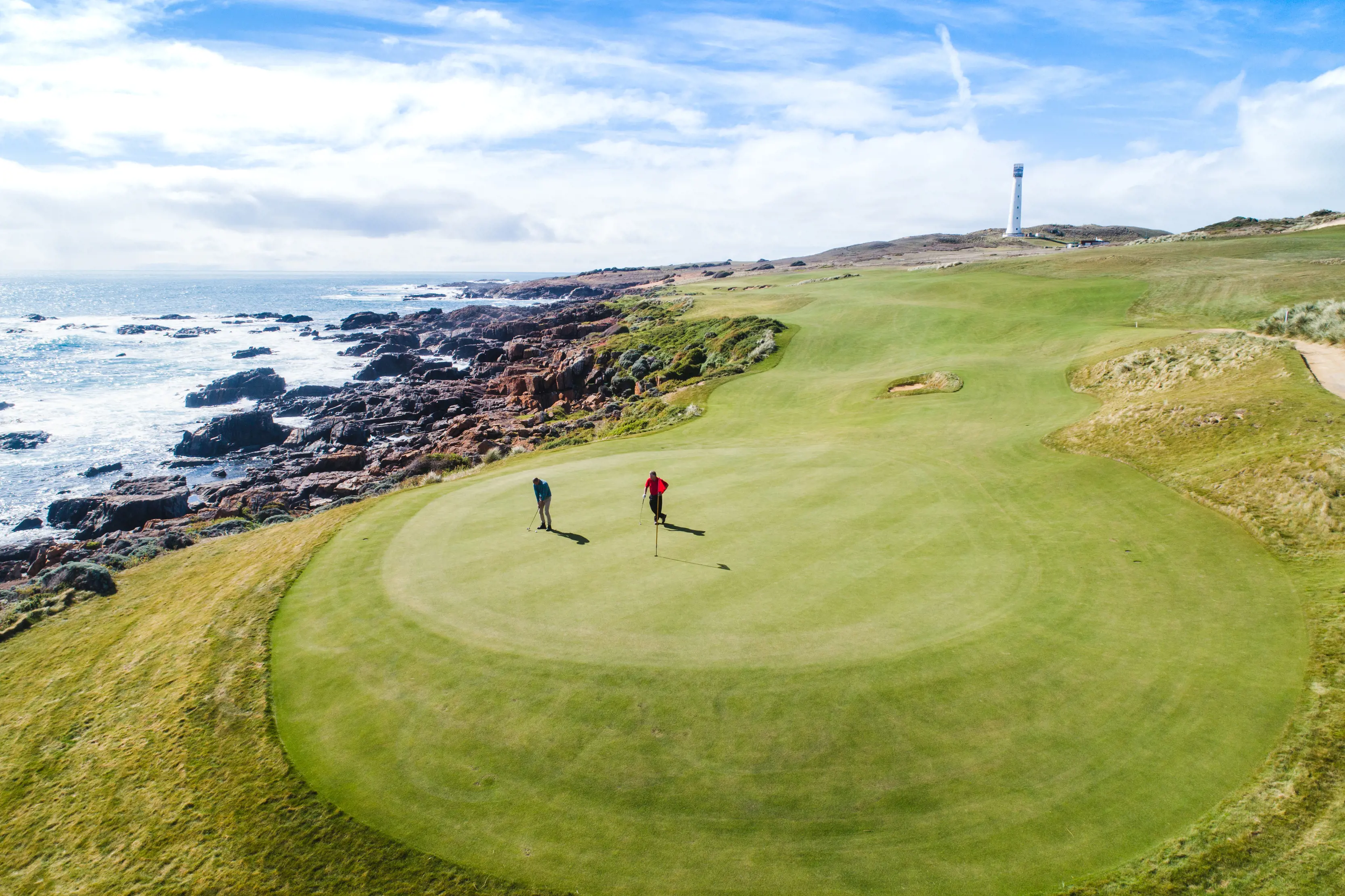 Wide aerial  shot of Cape Wickham Golf Course on King Island, with golfers in the foreground and the lighthouse in the background.