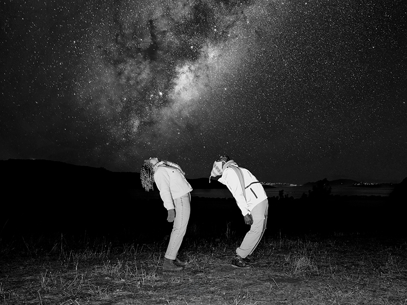 Two people arch their backs and look up into the night sky at the milky way.