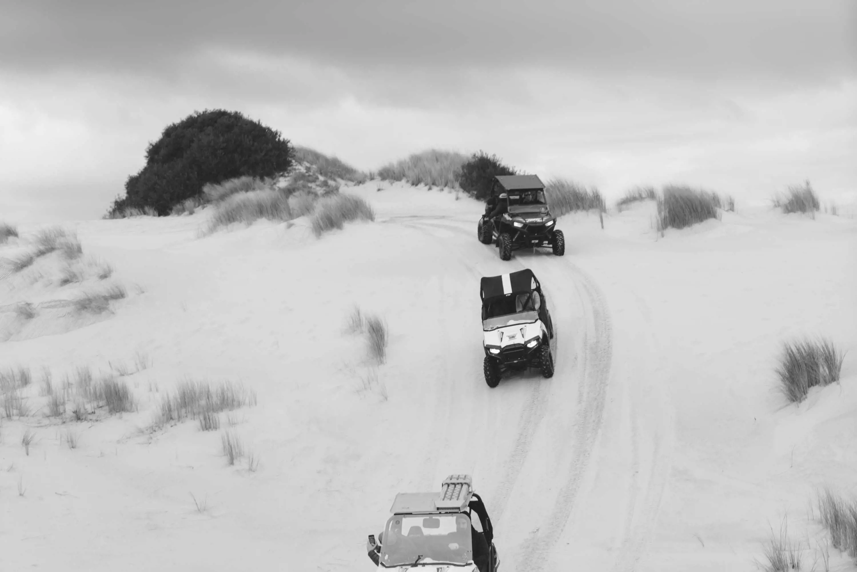 Three small, open-top all-terrain-vehicles drive down a sand dune.