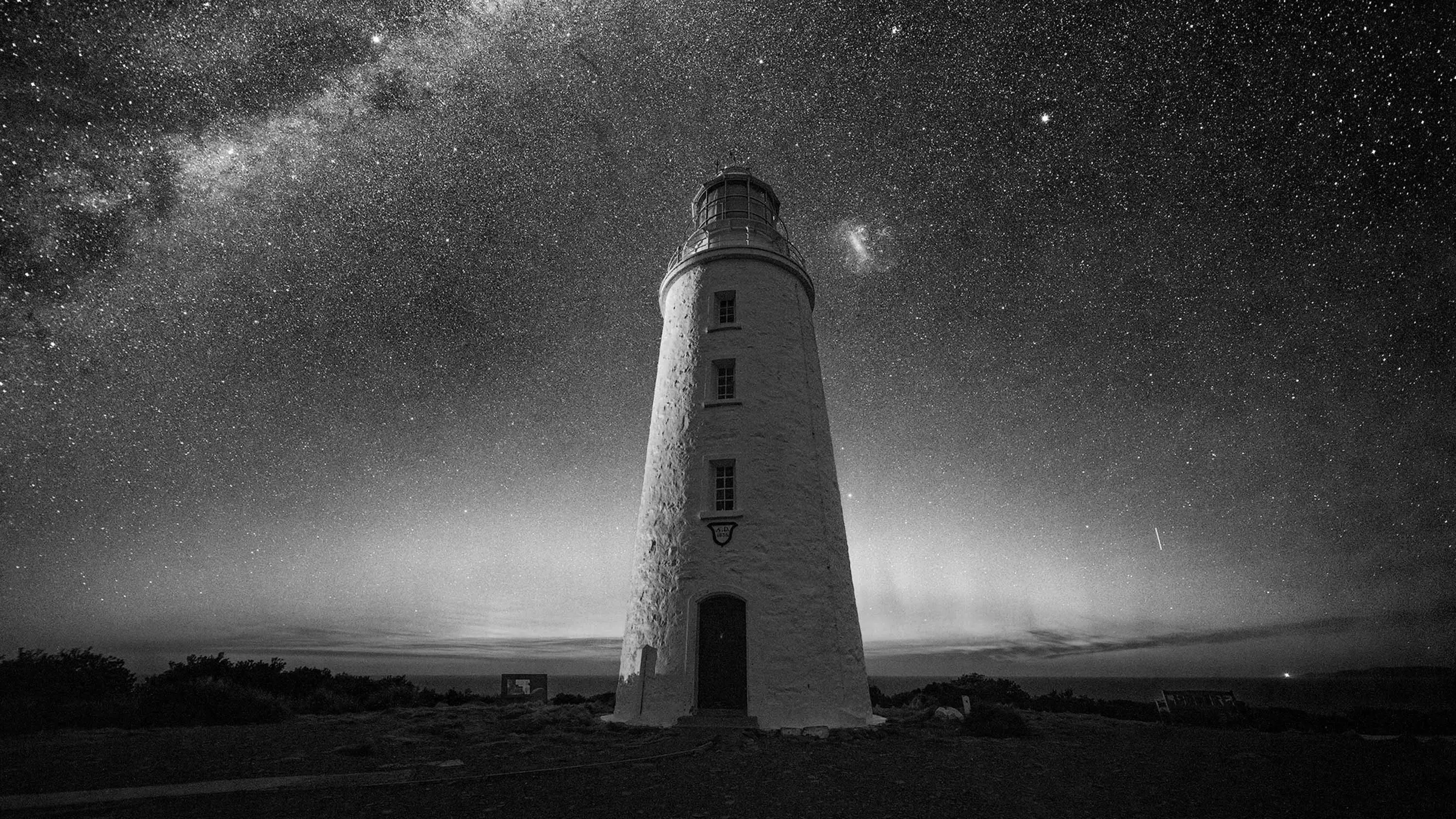 A lighthouse made of brick and painted white stands against the night sky, full of stars.