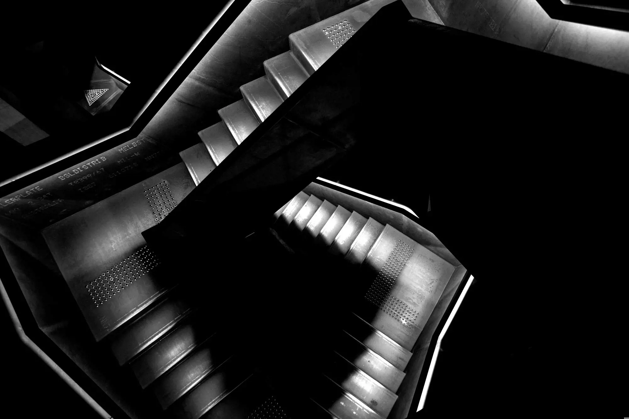 A industrial staircase made from iron sheets illuminated by led lighting descends into a dark basement level at Mona.