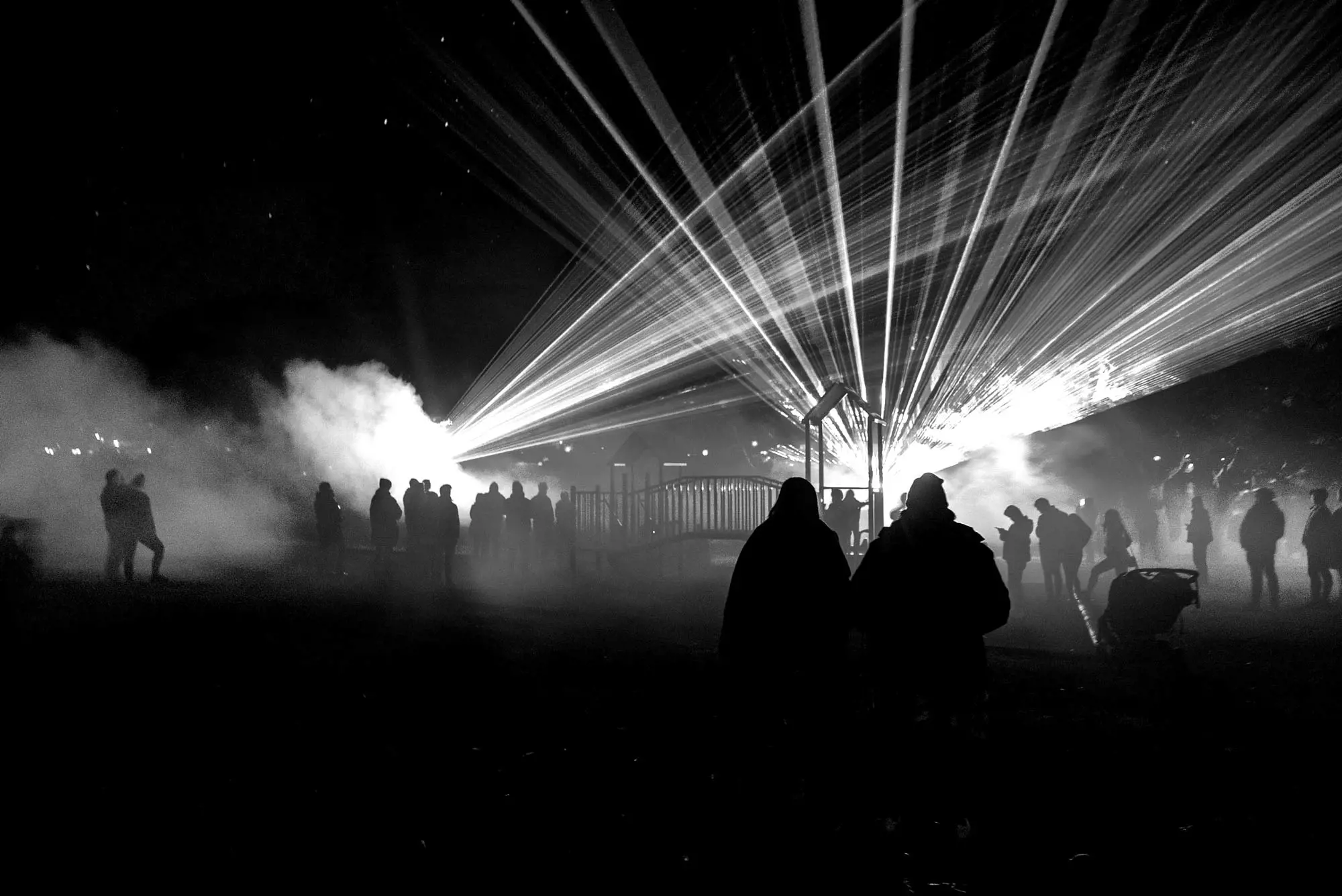 A couple stand in a park lit mysteriously by the laser lights that are cast over their heads.