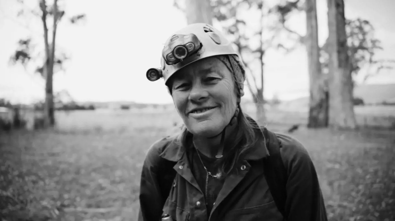 A portrait of Deb, wearing a hardhat with light and dressed in hard-wearing clothing.