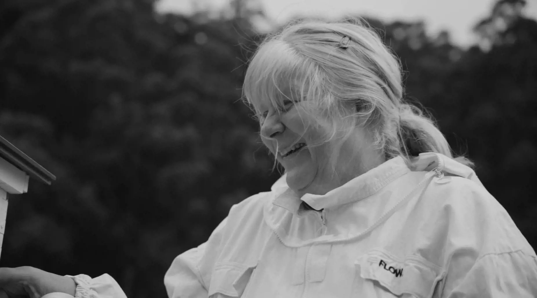 Lisa Britzman smiles stands next to a white beehive and watches the bees.