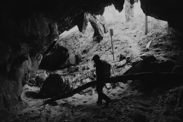 A figure walks in the base of a rocky cave system illuminated by the light of an overhead opening.
