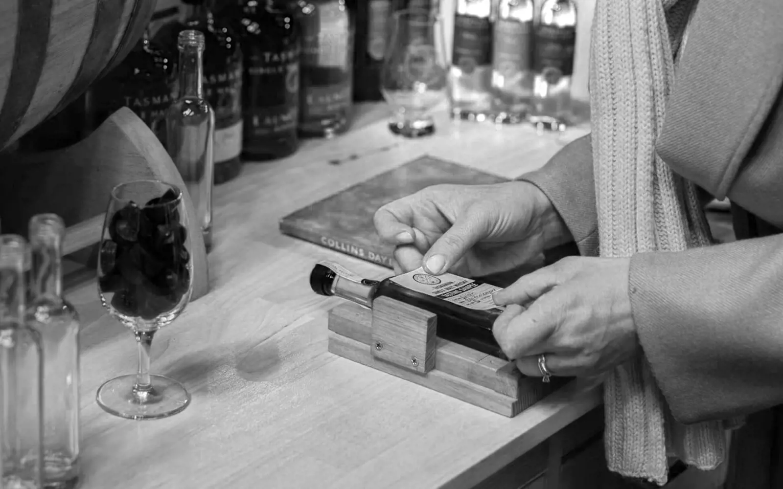 A person is carefully placing a label onto a small bottle of whisky.