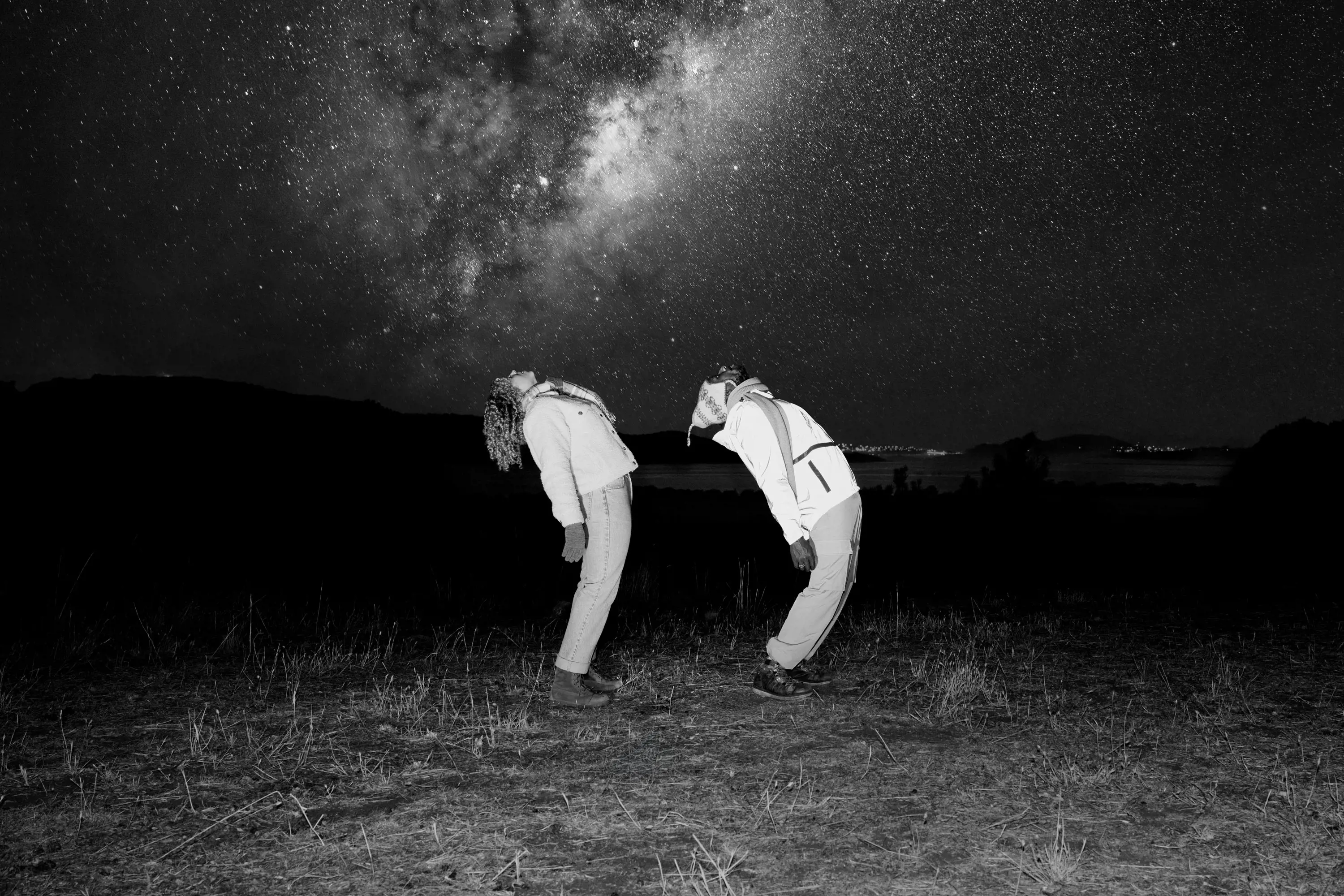 Two people arch their backs and look up into the night sky at the milky way.