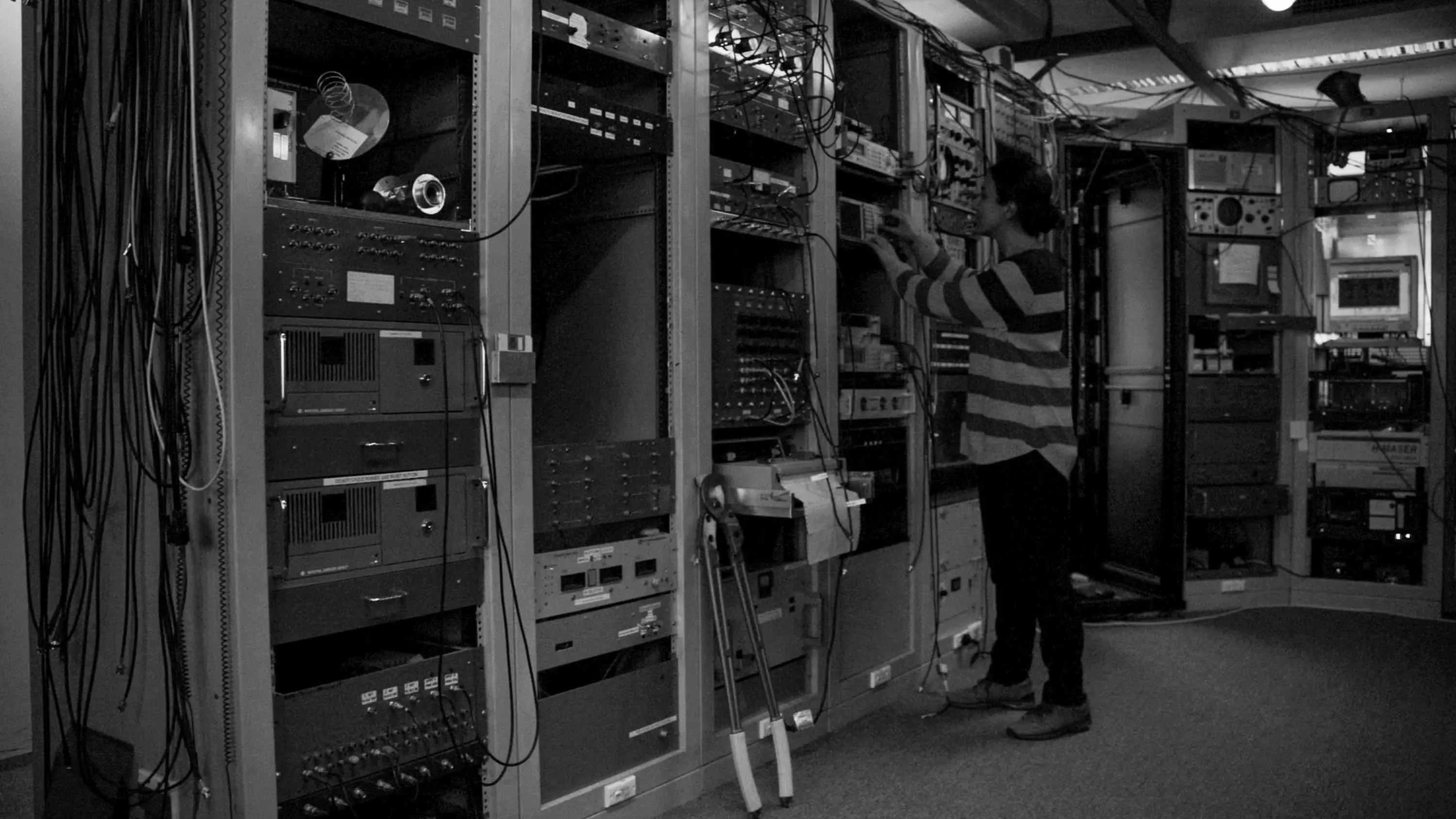 A woman stands next to racks of electronic measuring devices in a computer laboratory.