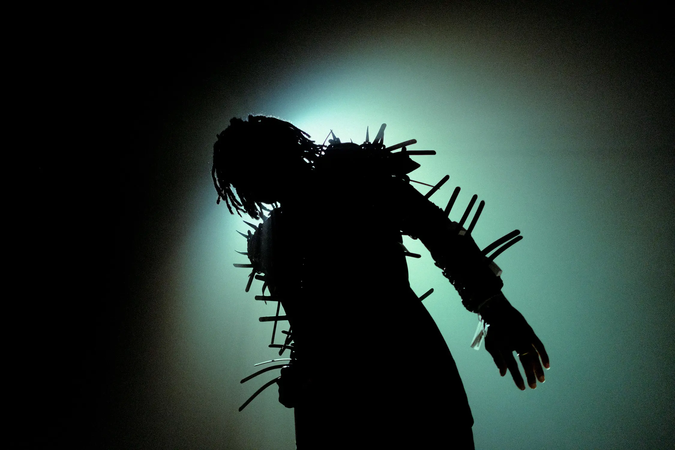 The silhouette of a man with dreadlocks dressed in an armour-like garment, covered in spikes.