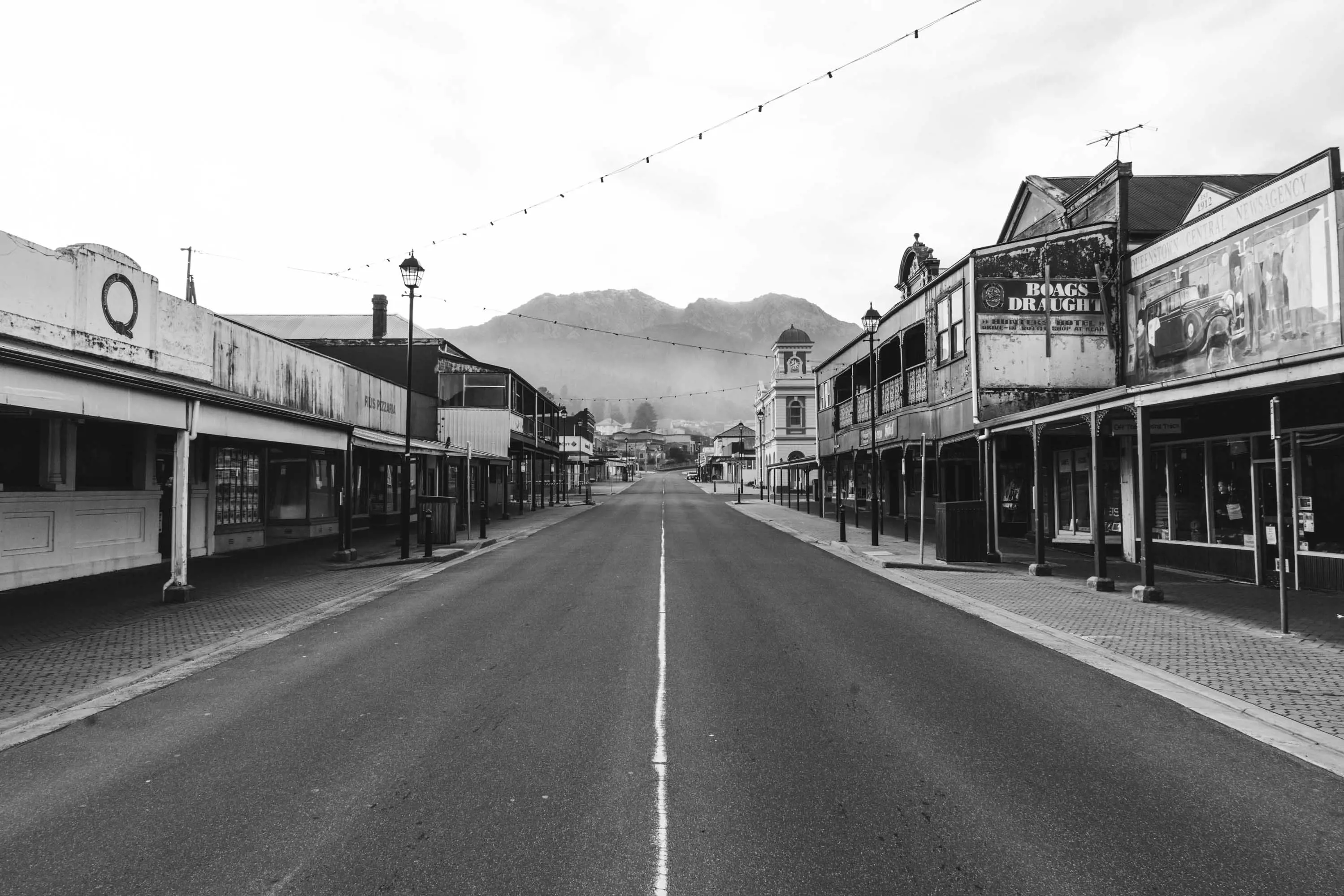 A wide street cuts through a quiet town with misty mountain in the background.