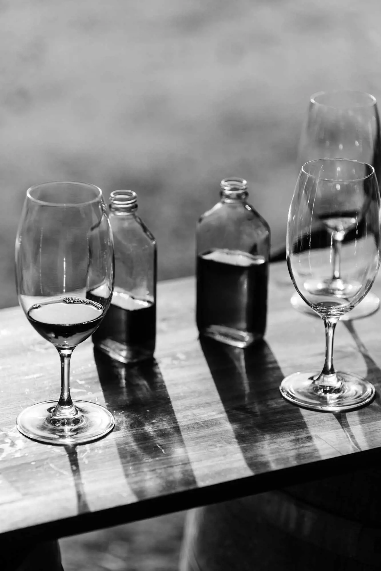 Wine glasses and small bottles of water sit on a wooden bench in the sunlight.