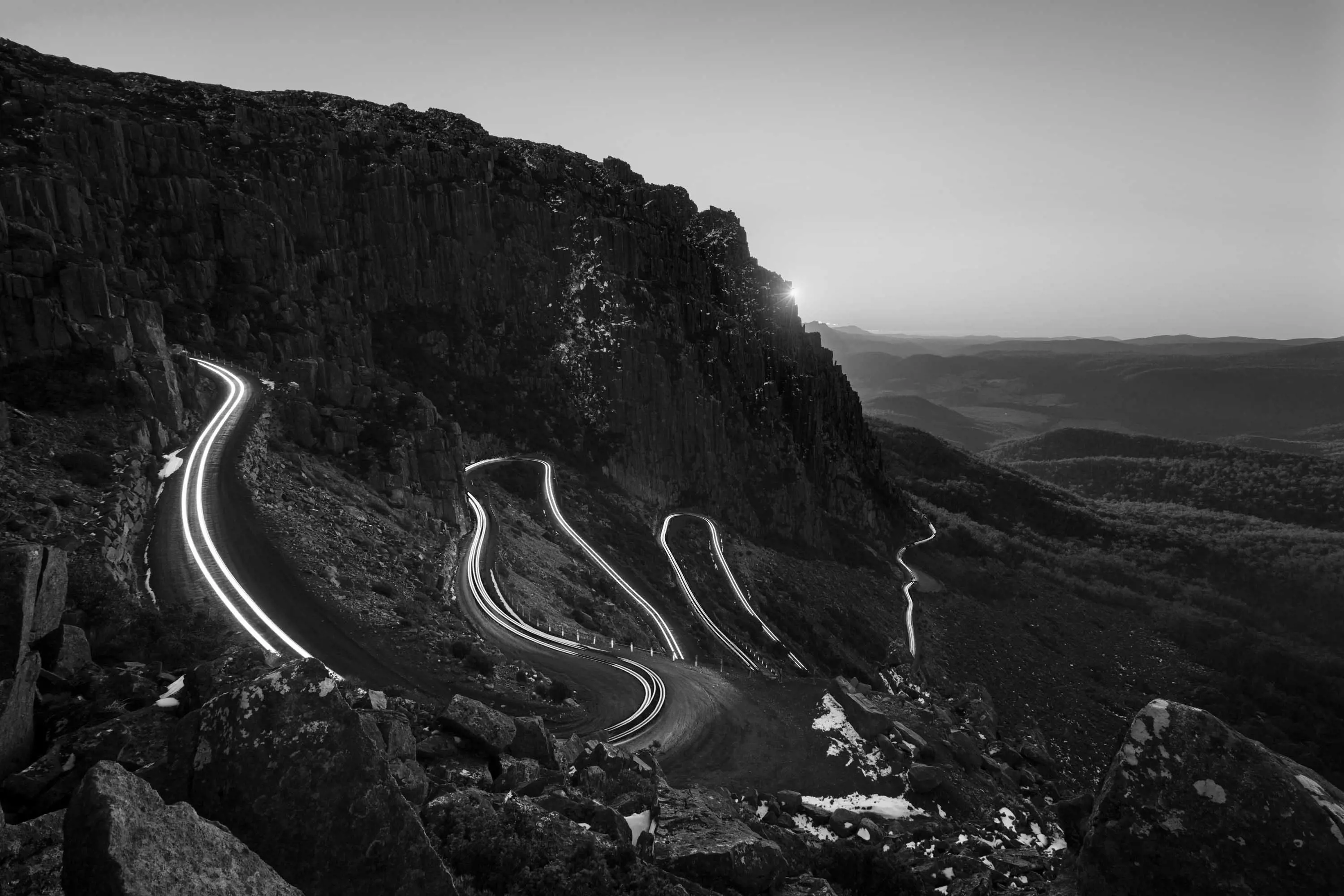 A narrow road winds up a steep mountain face. The long-exposure photograph capturing car's lights as they travel up and down.