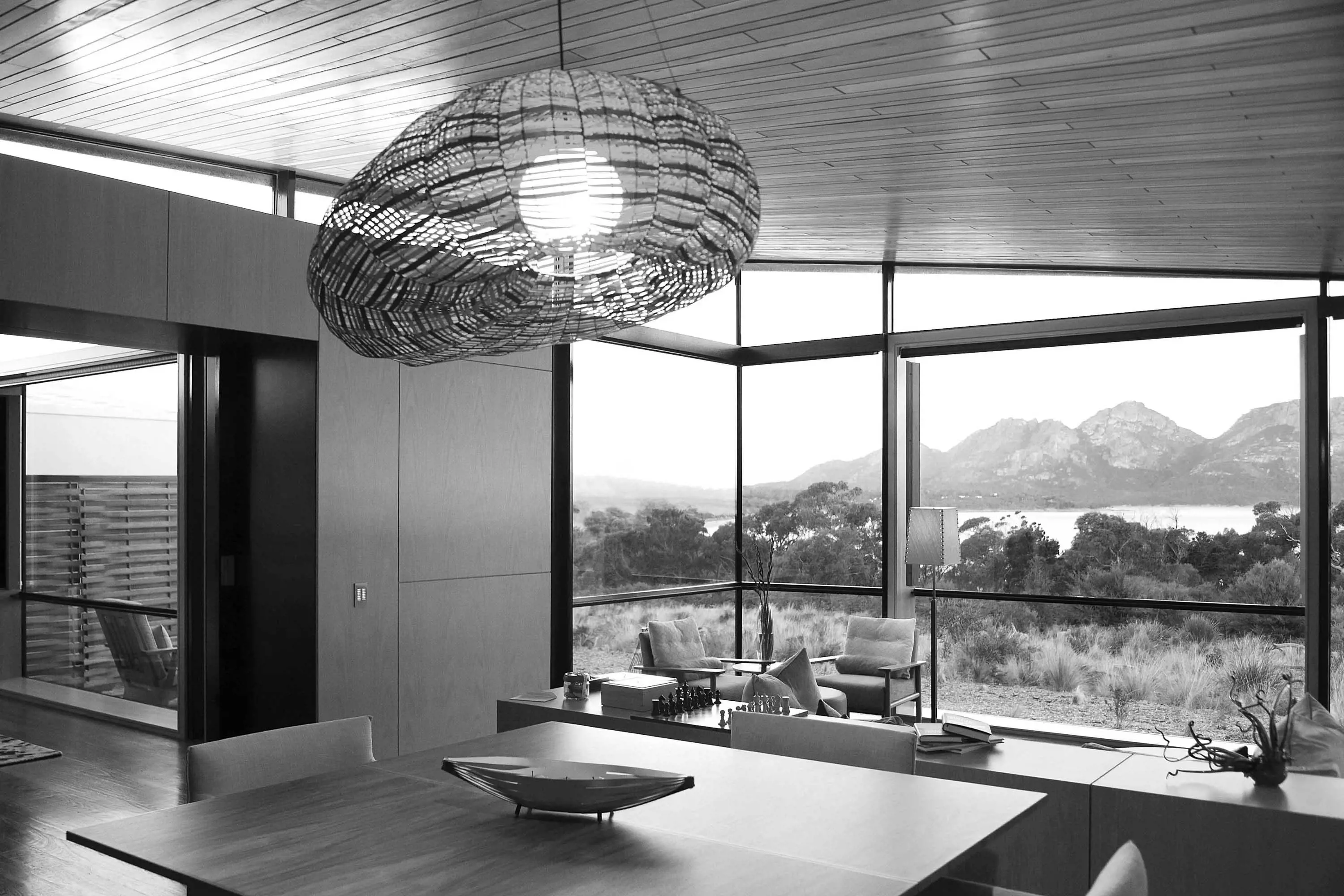 A dining table in an expansive room with tall windows with views of mountains in the distance. 