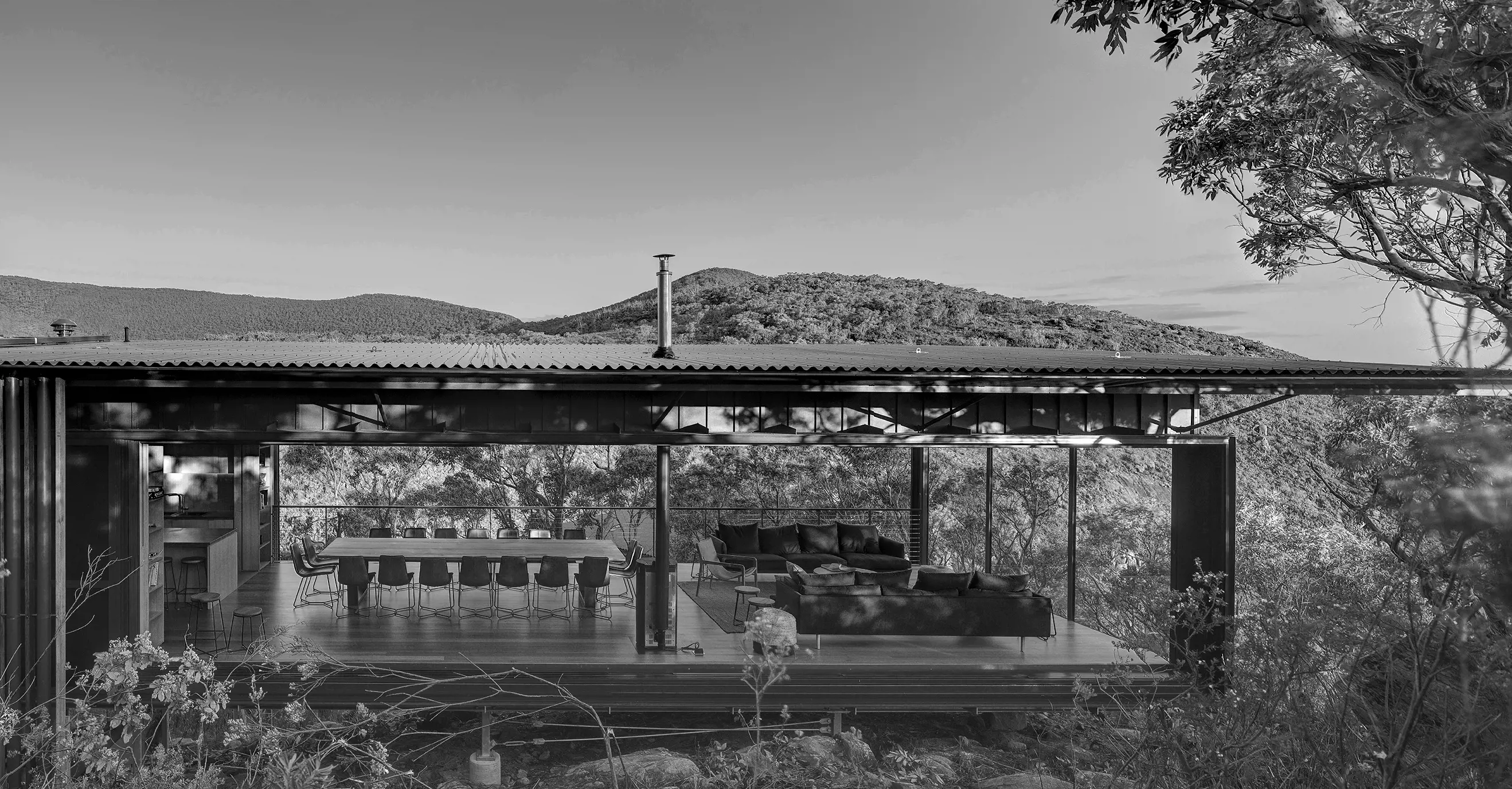 A large, corrugated steel verandah extends from a low-profile building set in the bushlands near slopping hills.