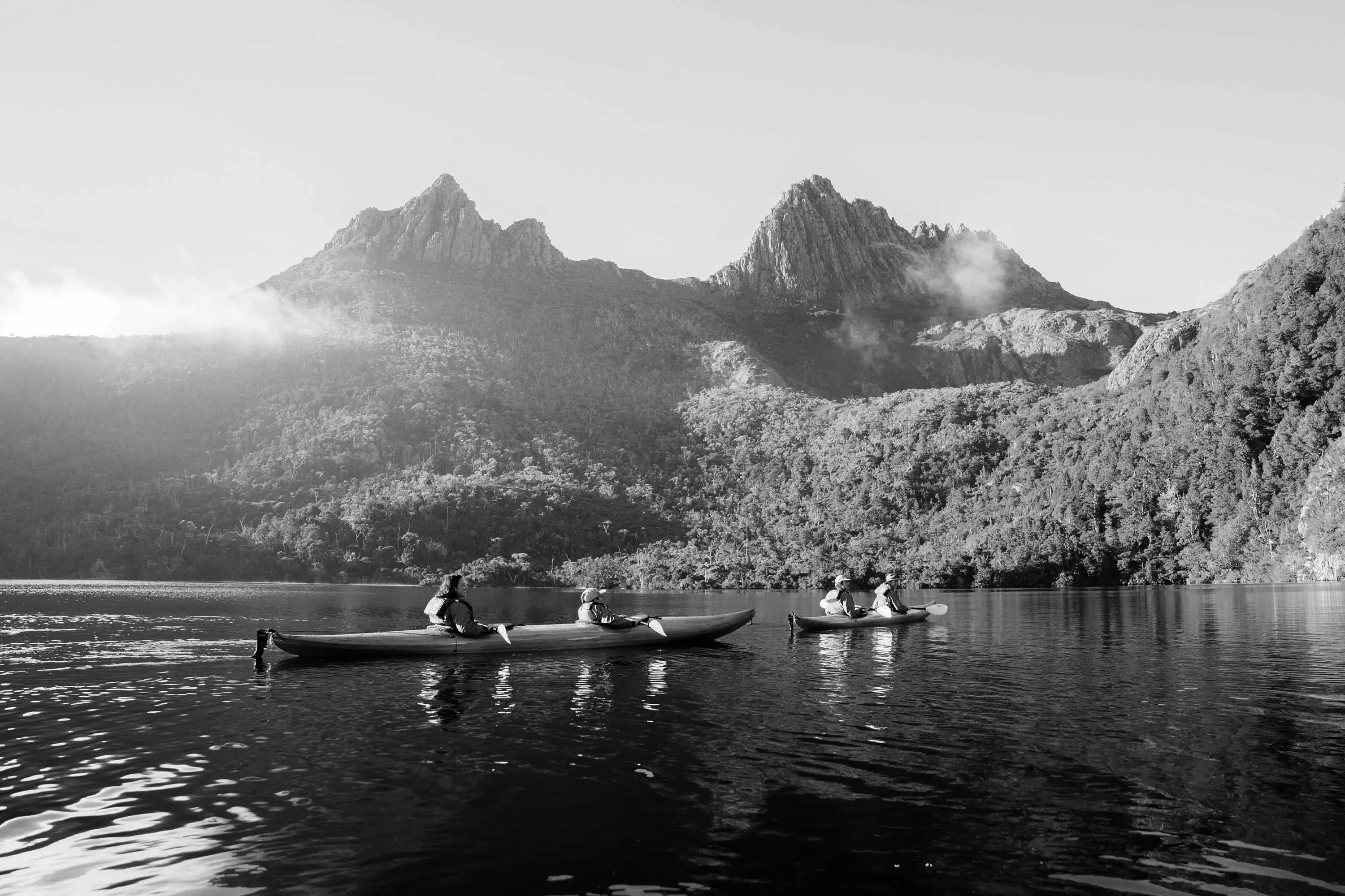 Two, two-person kayaks float gently on still waters of a lake below the large rocky peaks of Cradle Mountain 