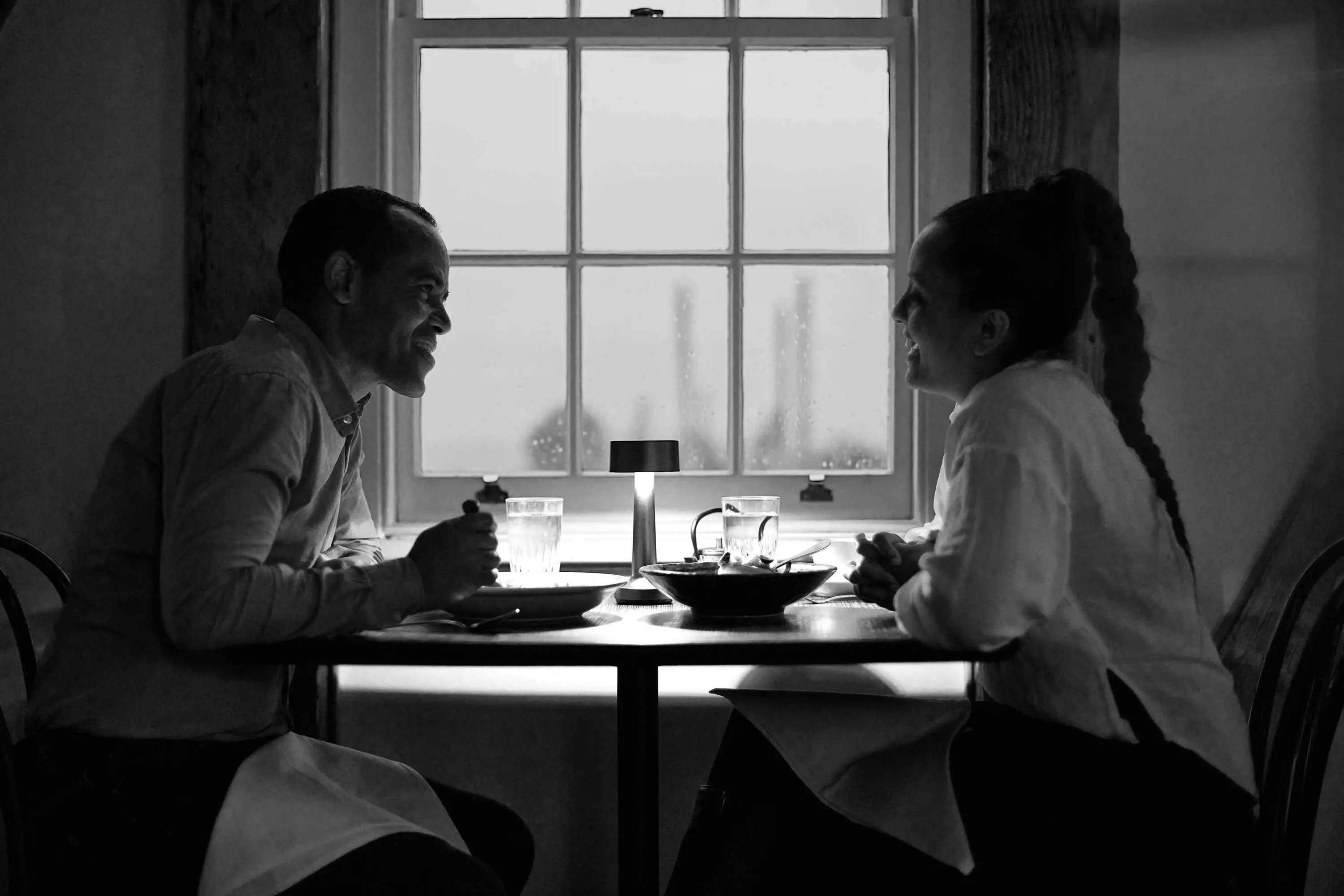 A couple sit at a table by a window in a restaurant.