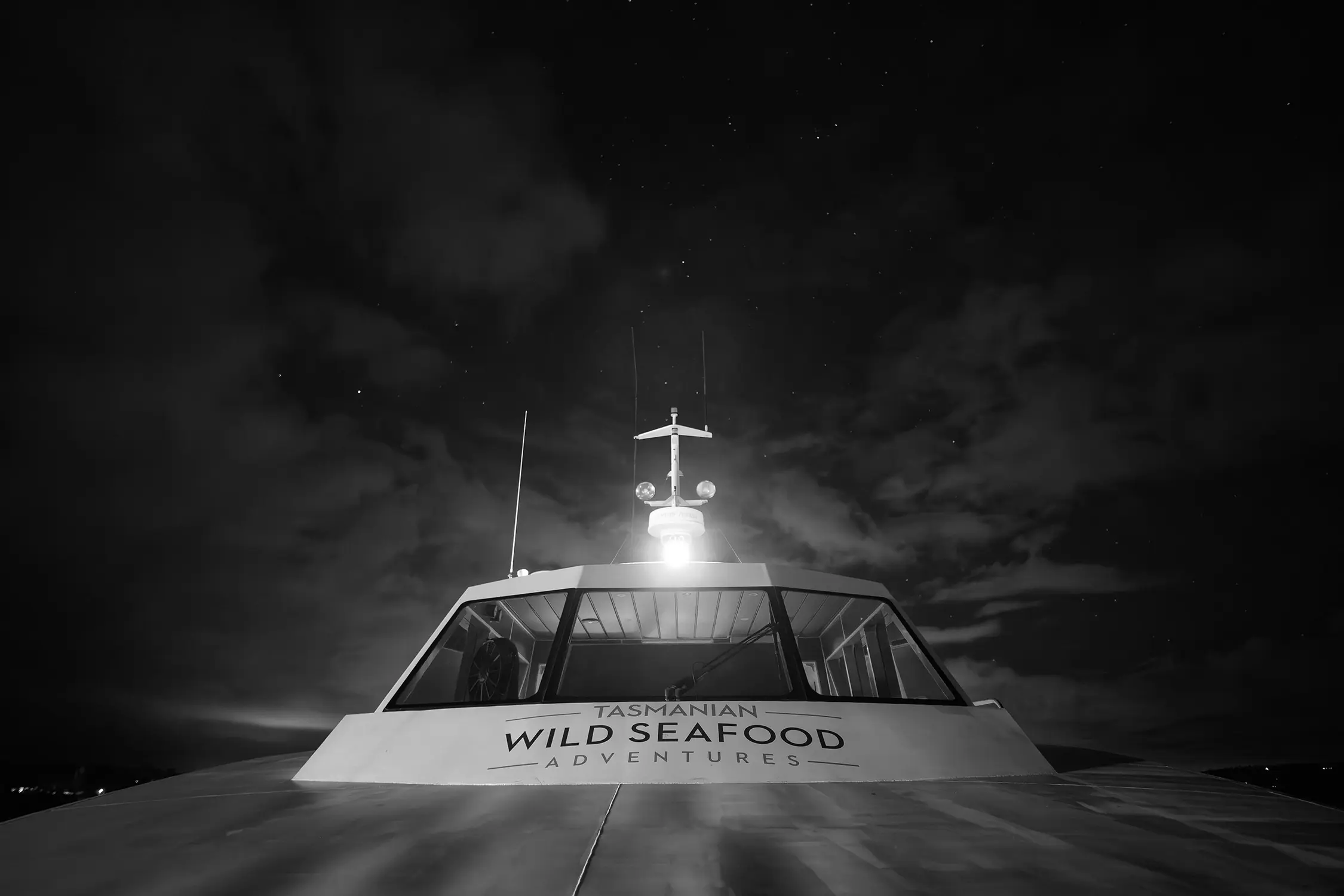 Looking up at the helm of a boat, with the dark night sky above it. The sign on the front reads 'Tasmanian Wild Seafood Adventures'.