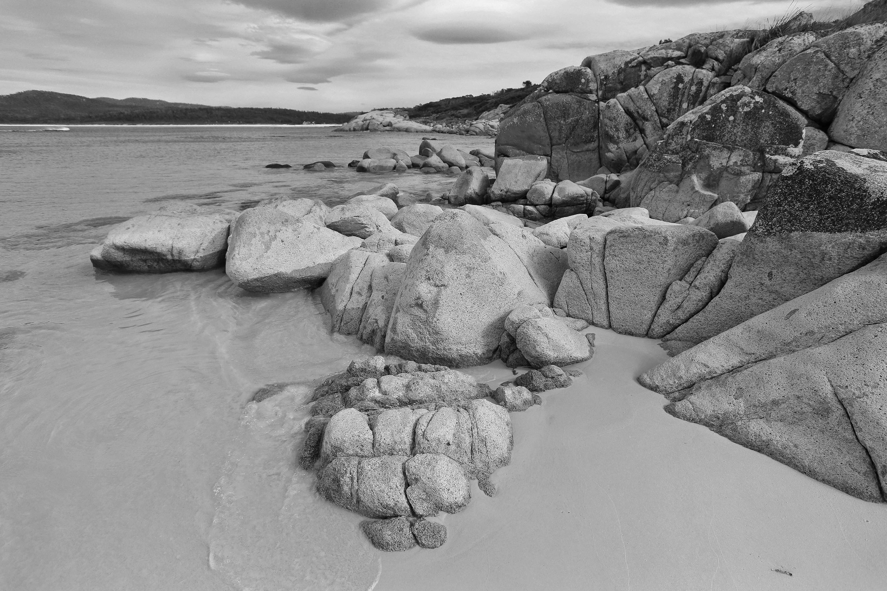 Large, lichen-covered angular rocks lead into the clear, still waters on the east coast of Tasmania.