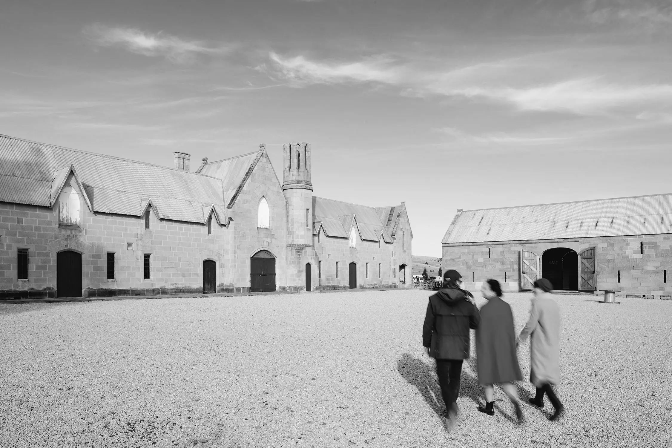 Three people walk across the gravel courtyard of a historic estate, with the sandstone buildings surrounding them.