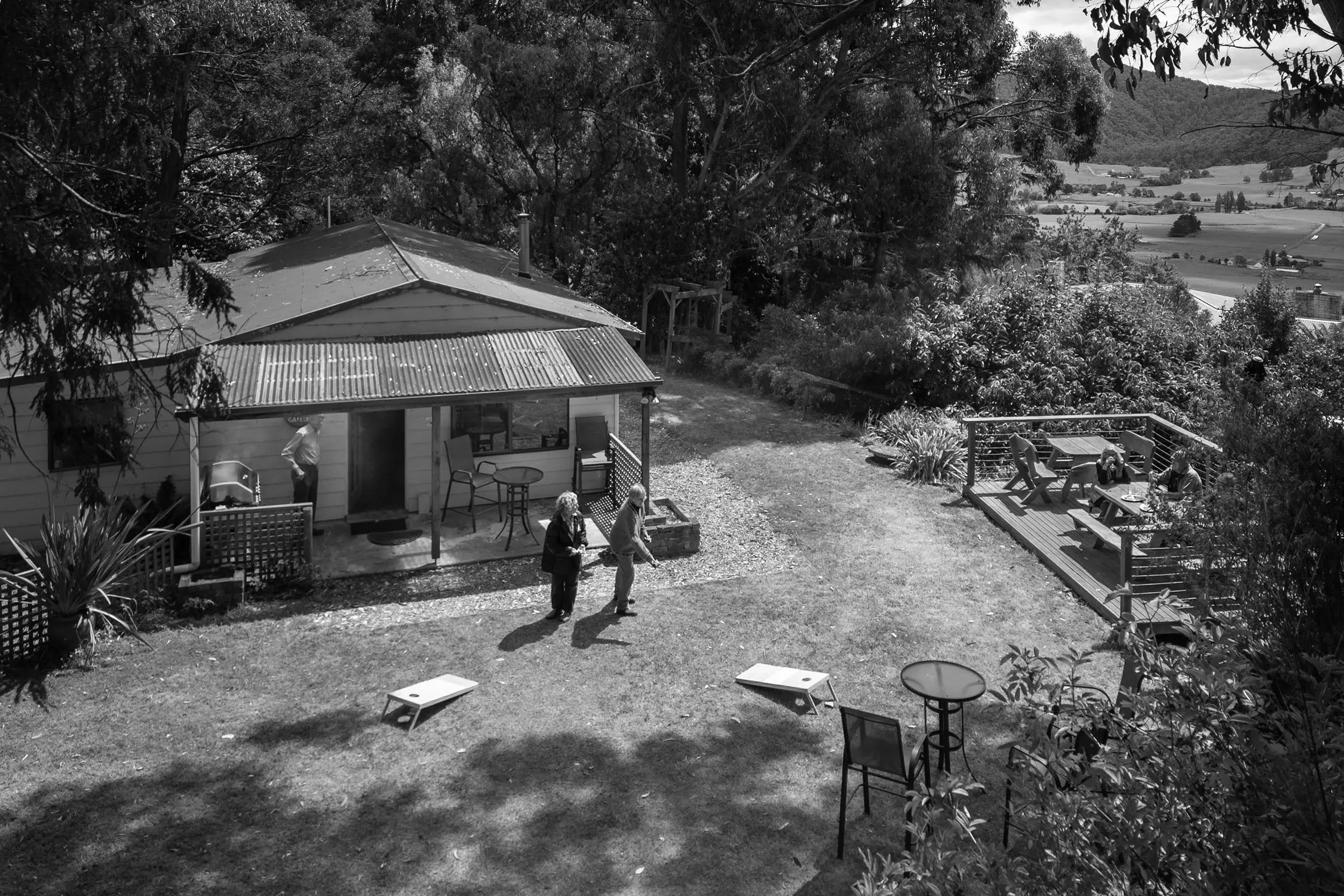 Looking down into the outdoor area of a small building nestled into treetops, with picnic tables and a game of cornhole being played.
