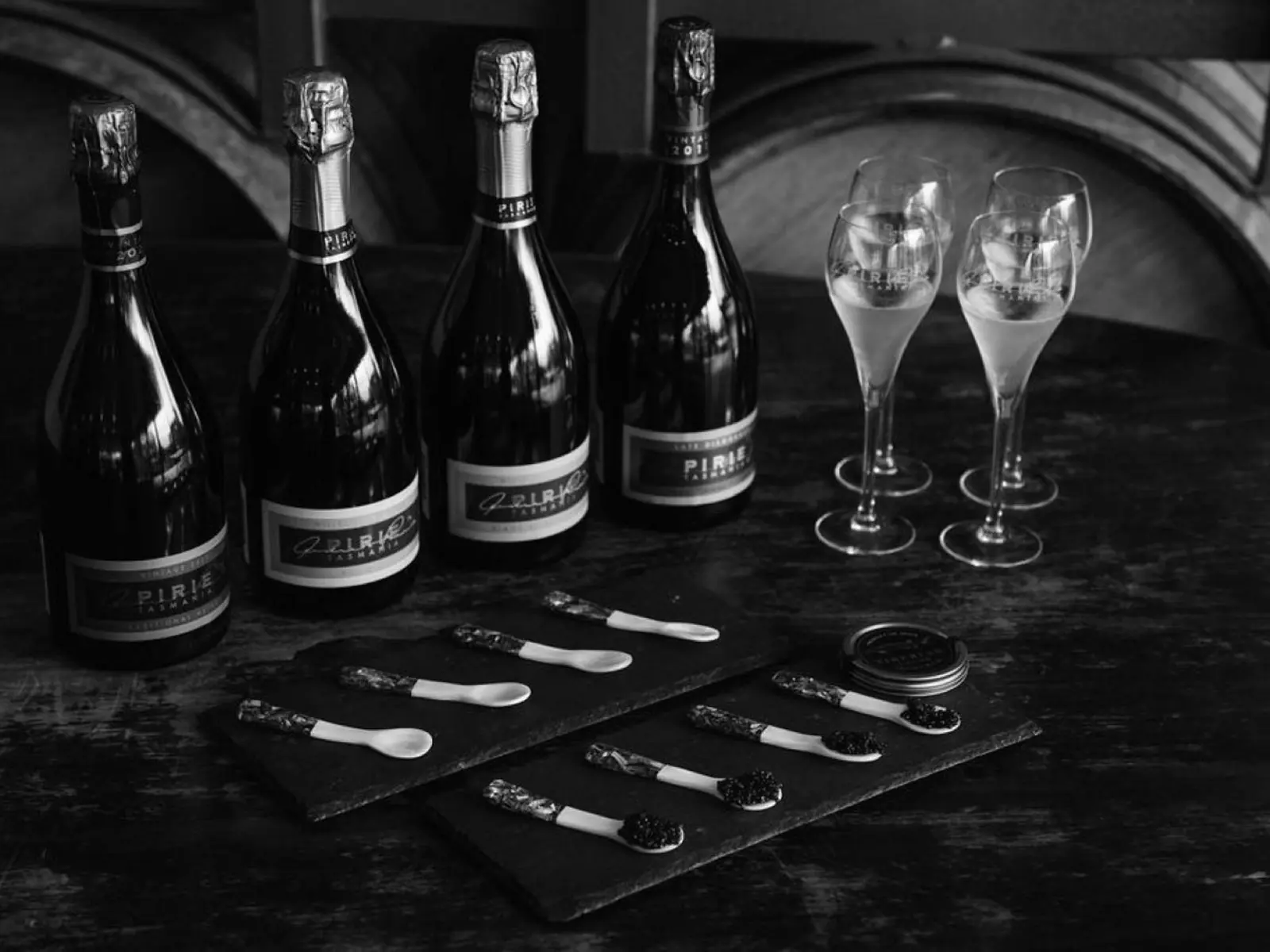 Bottles of sparkling and glasses sit on a marble counter top, along with trays of small spoons loaded with rich caviar.