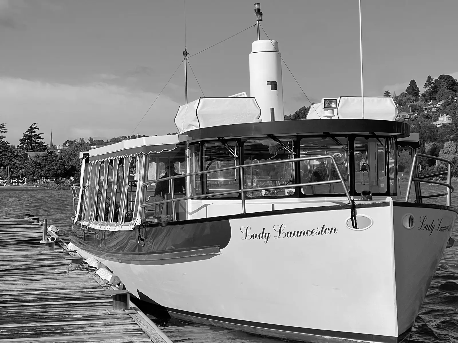 A river cruise boat is moored alongside a jetty. The cursive lettering on the bow reads 'Lady Launceston'.