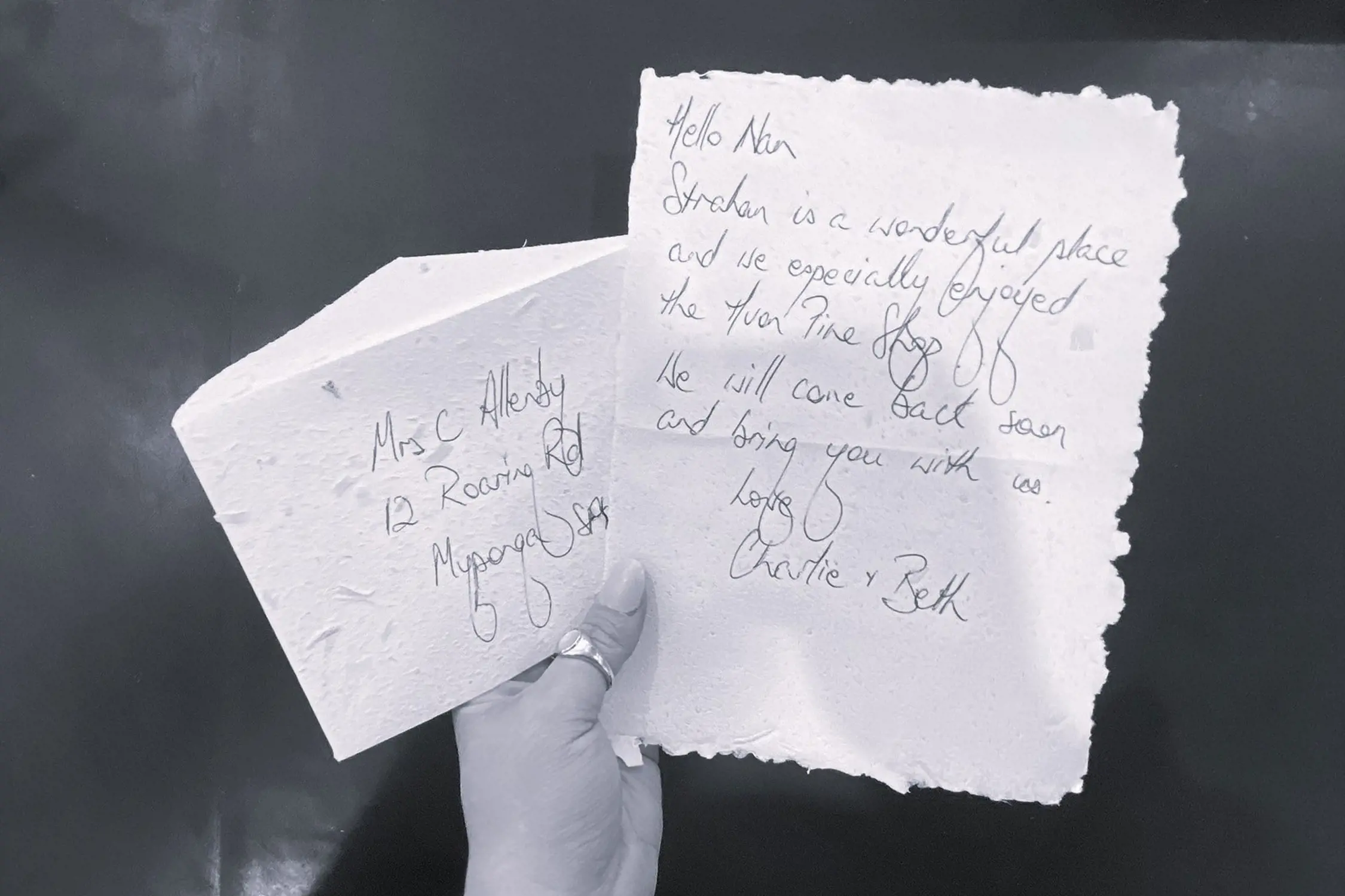A handwritten note and envelope held in a hand with an address and a message about visiting Strahan.