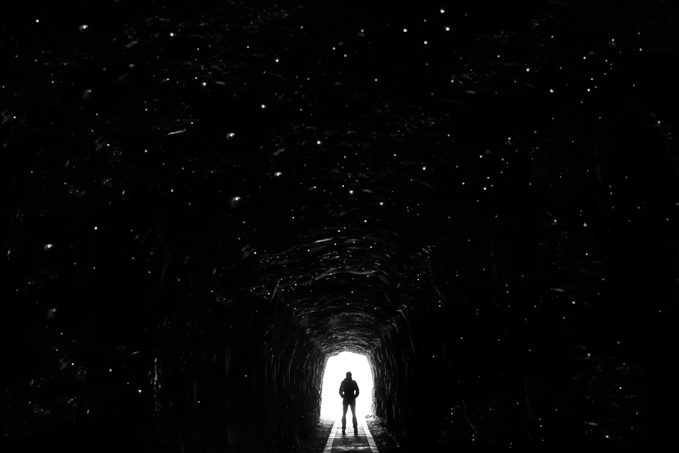 Silhouette of a person standing at the bright entrance of a dark tunnel, surrounded by darkness.