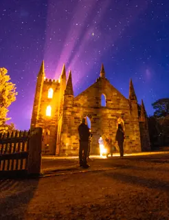 An old sandstone church is illuminated from within with yellow lights on a a night sky.