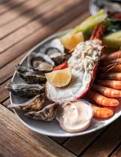 A platter of freah oysters, cooked prawns and half a lobster presented with sauces, lemon and vegetables.