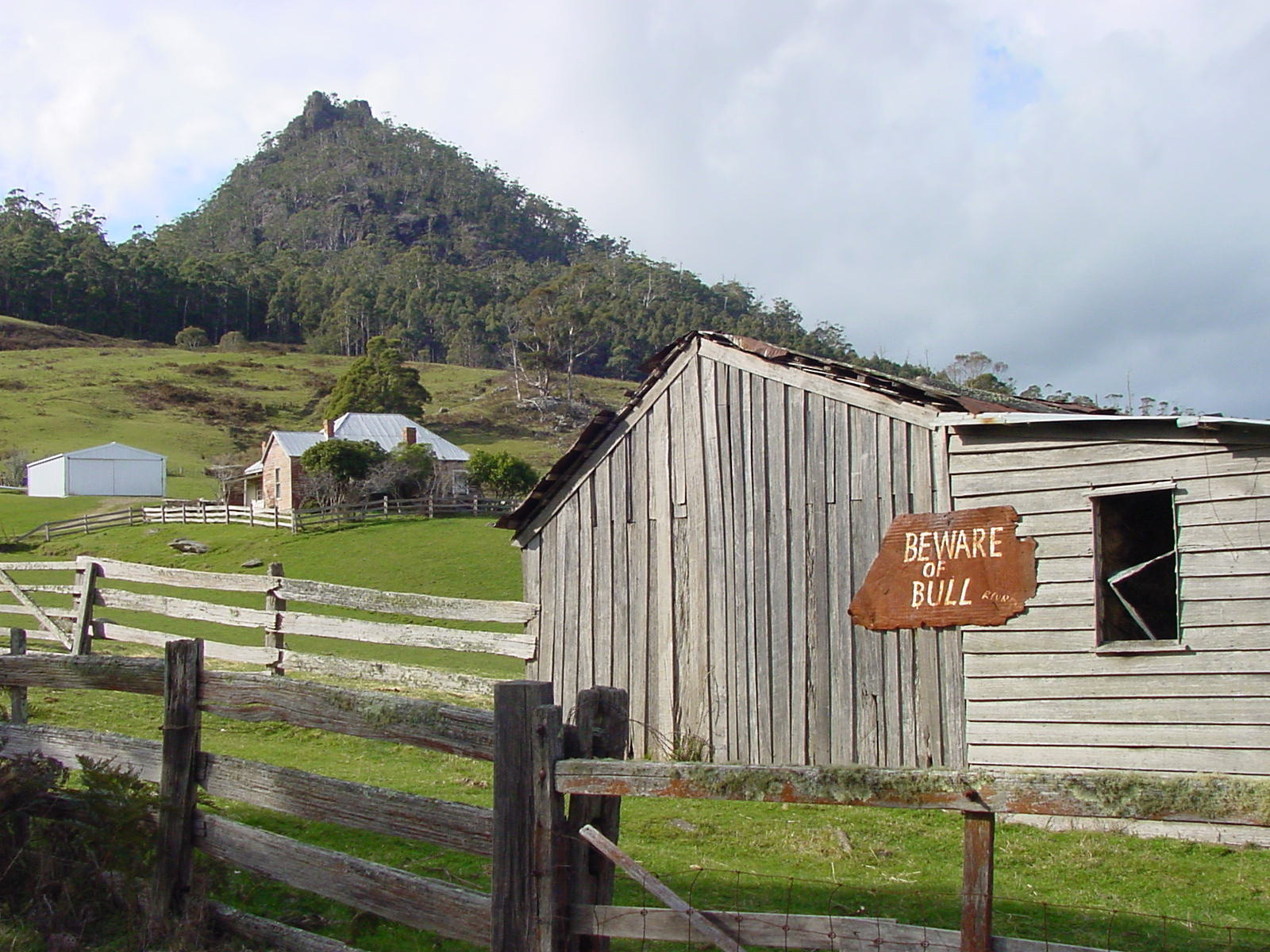 Close up image of St Marys Farm. The trees on the hill in the background and a sign on the farm door that reads 'beware of bull'. 