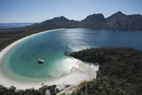 Stunning aerial image of Wineglass Bay on a clear, sunny day with crystal clear, blue water. Wineglass Bay Cruise boat is docked within the Bay.