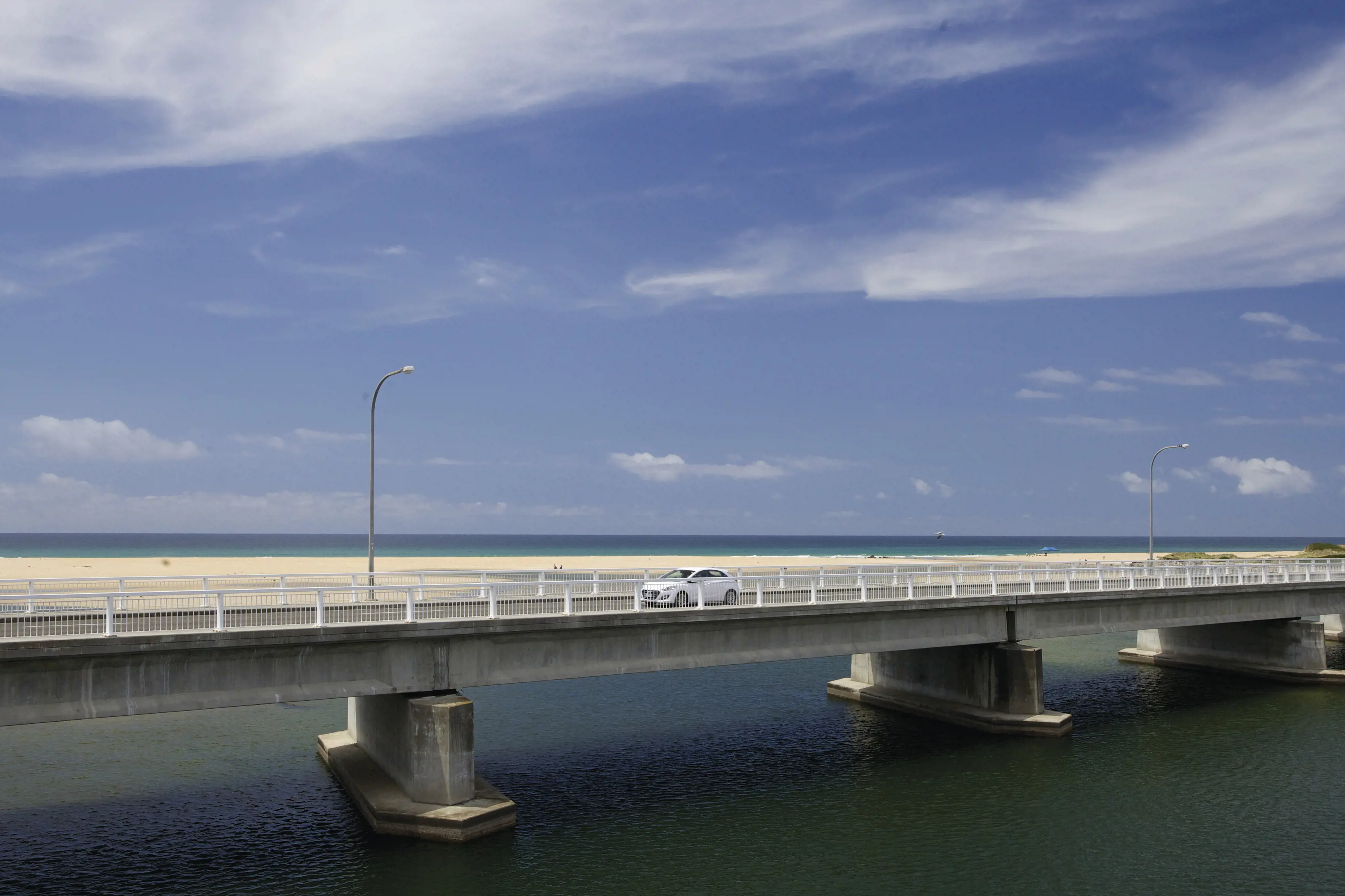 A white car drives across the bridge at Scamander, with white sandy beaches in the backdrop.