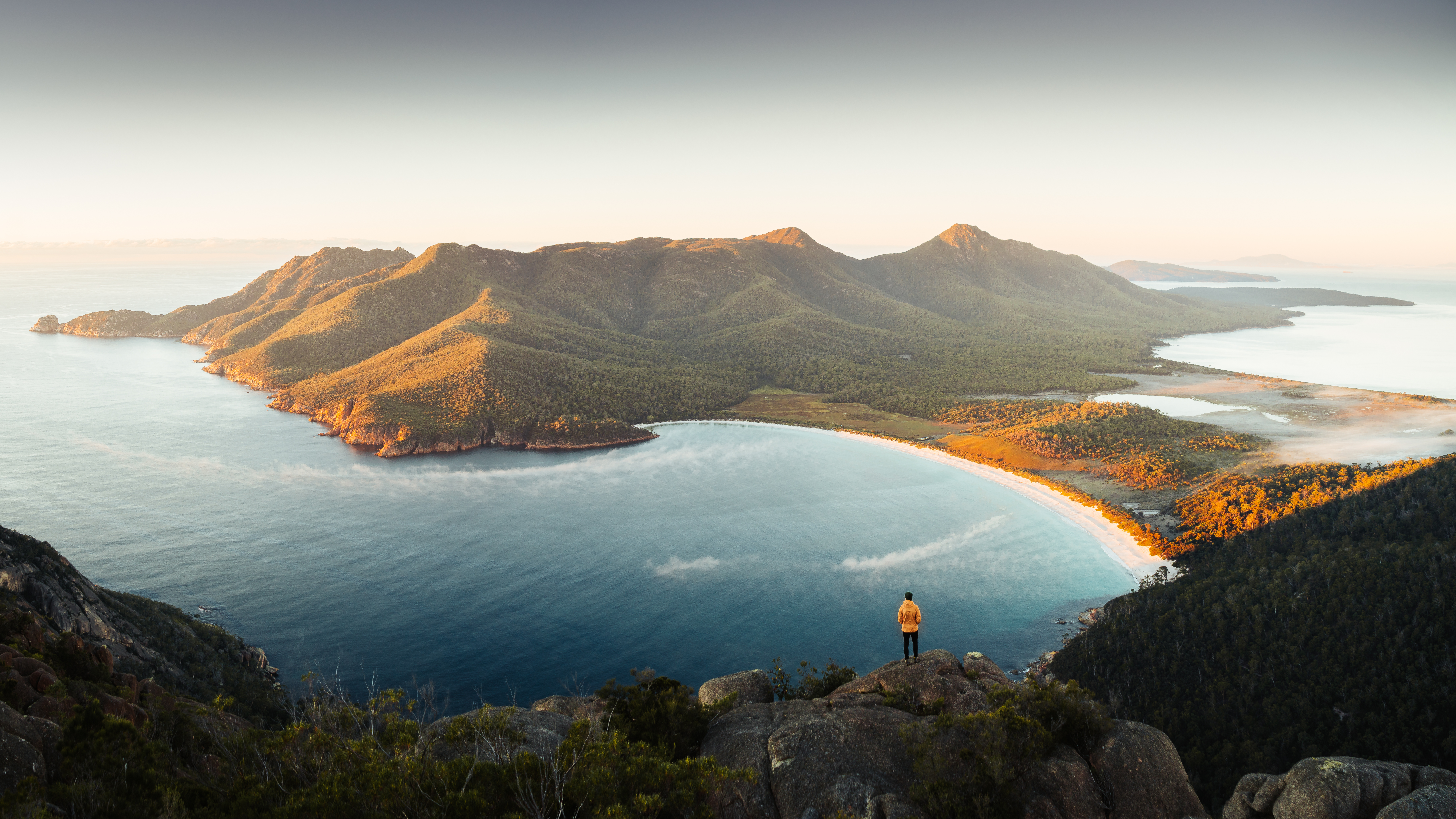 Aerial shot of Wineglass Bay, Freycinet National Park. A man standing on the cliff, looking out onto the water. 