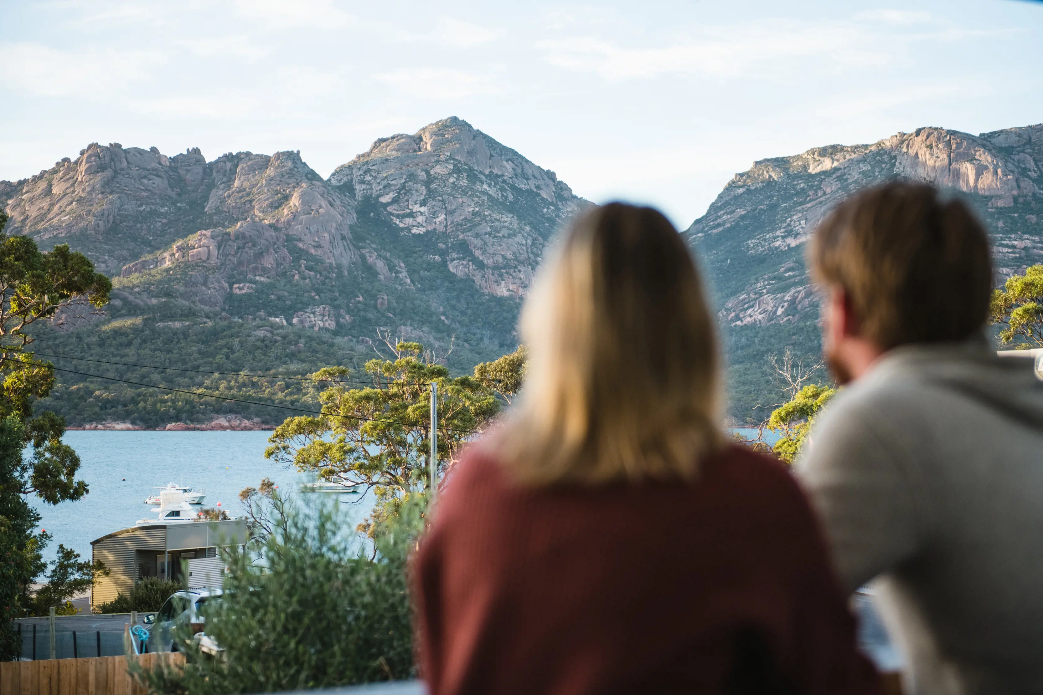 Image taken from behind a couple enjoying refreshments at Geographe Restaurant and Espresso Bar, with views of Coles Bay in the background.