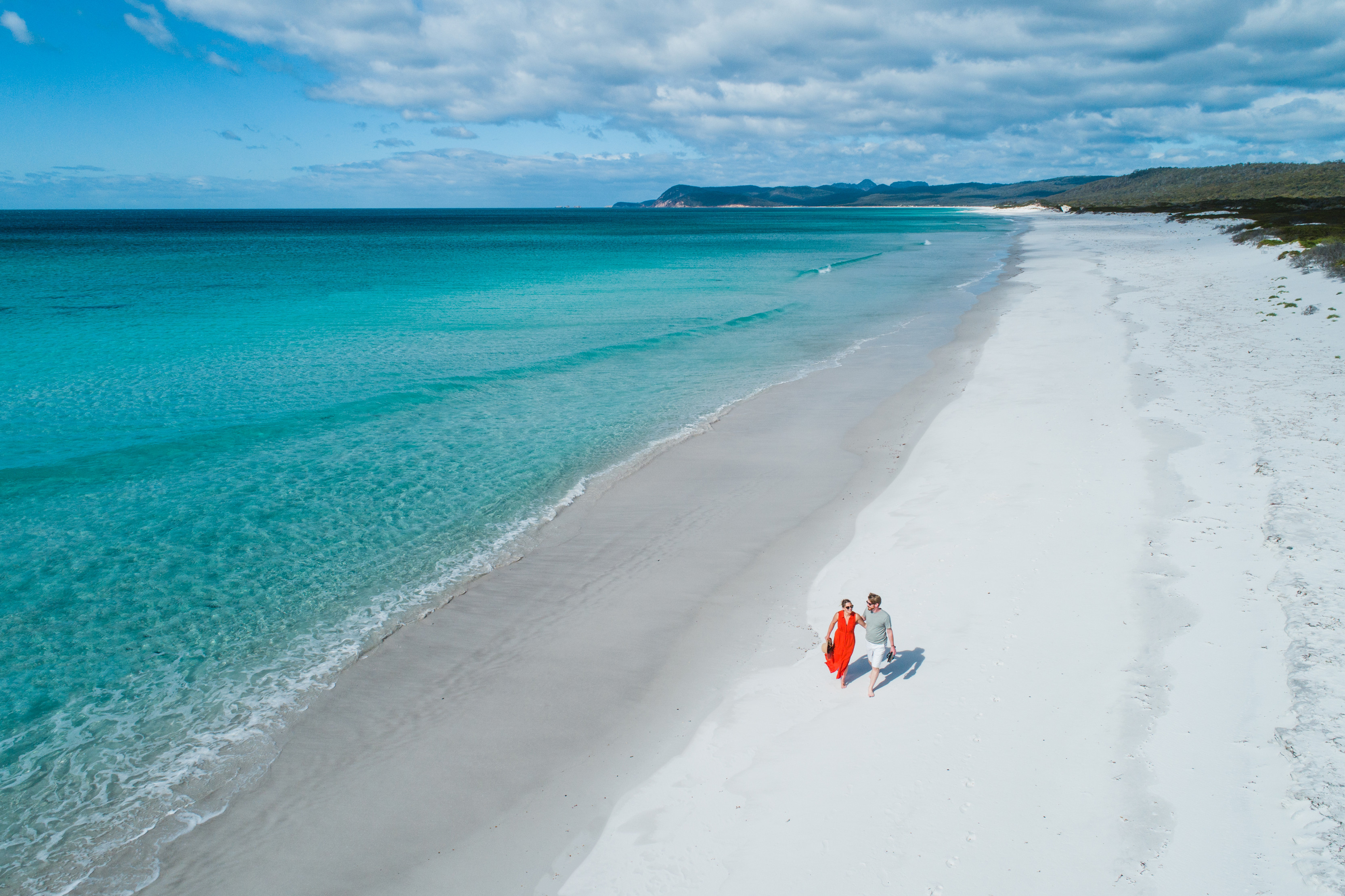 Two people walking along the white sand of Friendly Beaches, Freycinet National Park.
