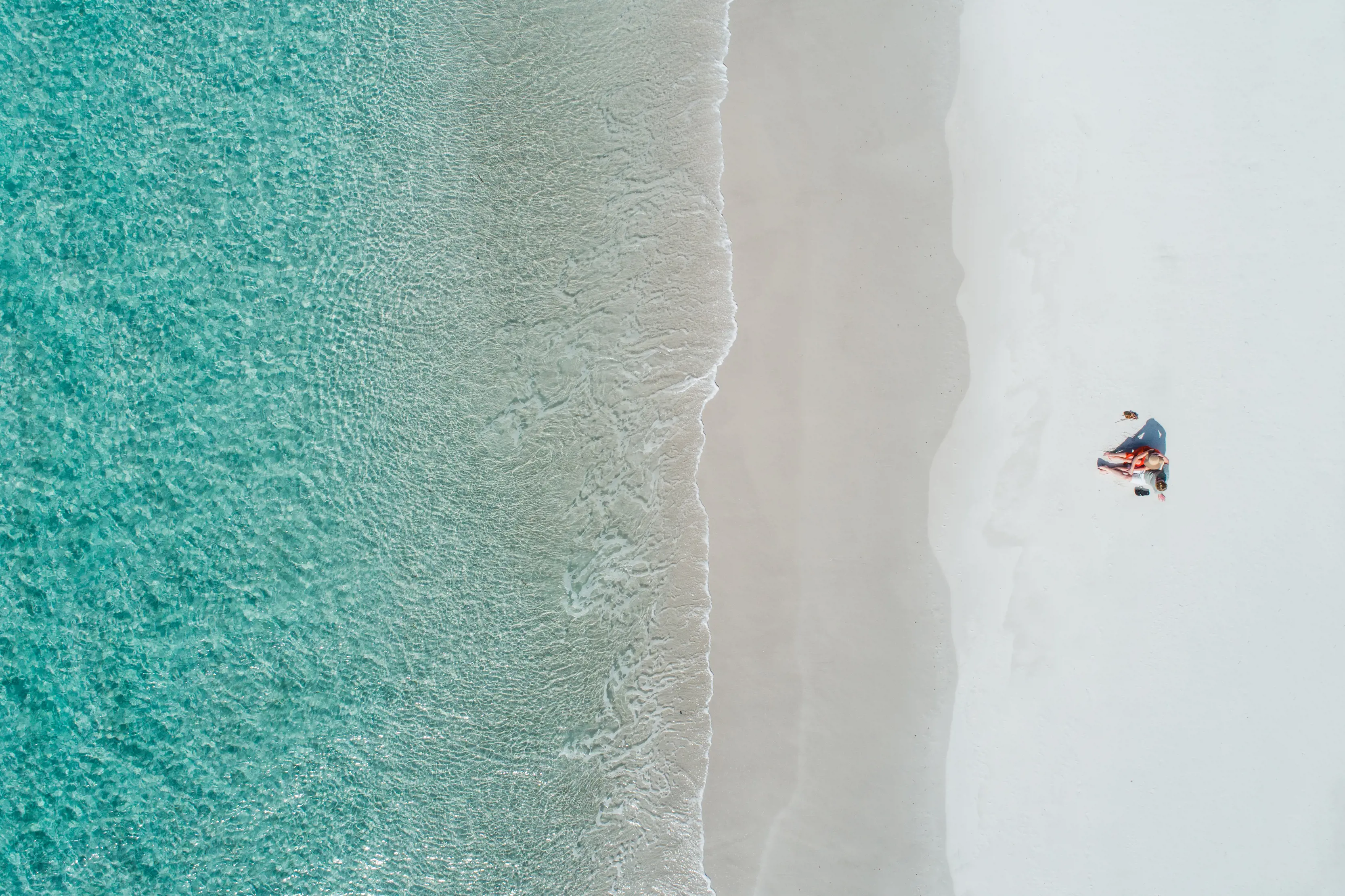 Top-down view of woman laying on the sand in front of clear water at Friendly Beaches, Freycinet National Park.