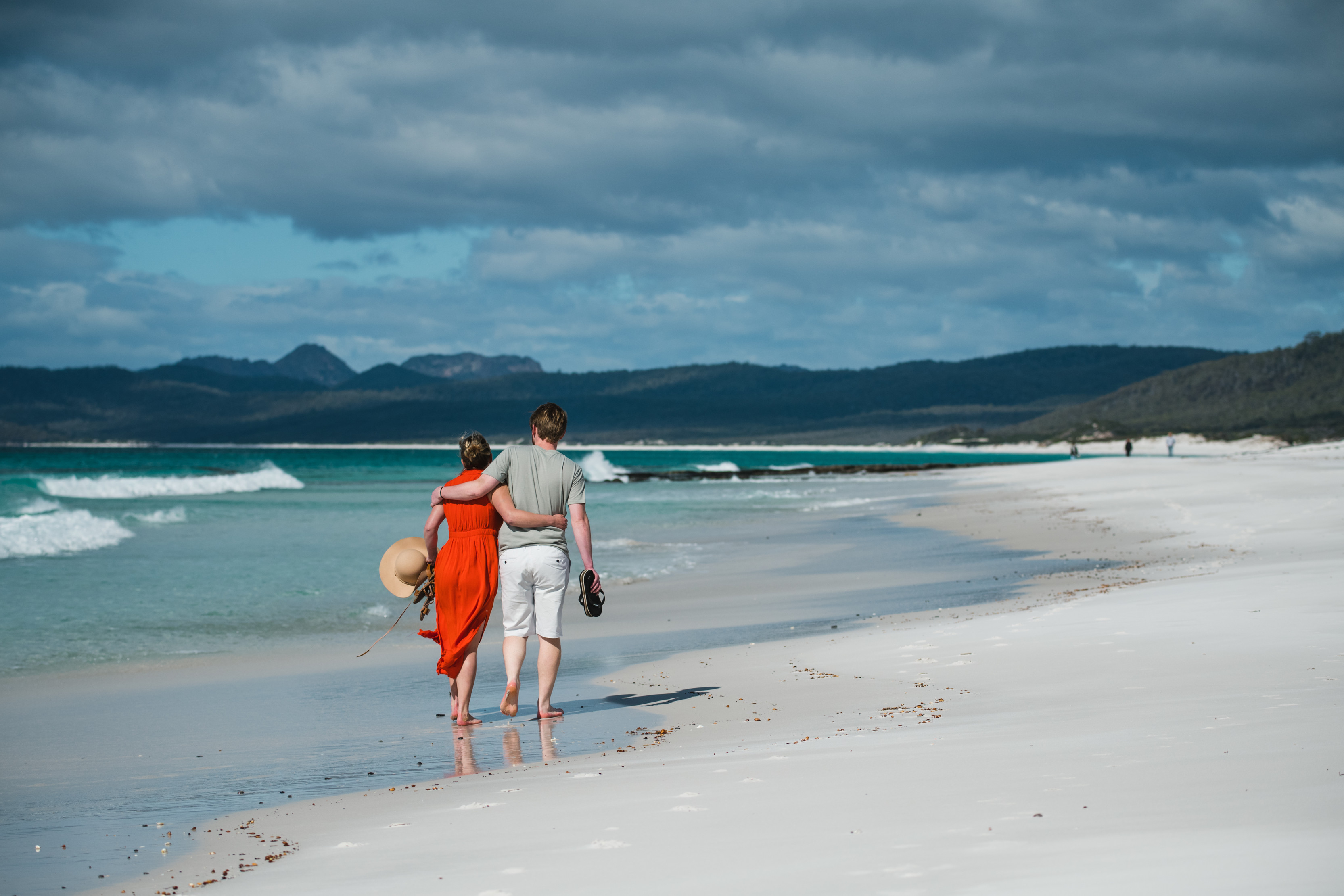 Couple walking along the beach. Girl in red dress. At Friendly Beaches, Freycinet National Park