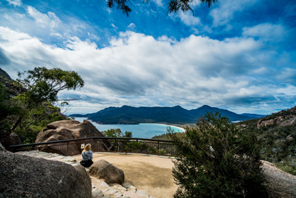 Image of a woman sitting on a rock, in the lookout spot of the Wineglass Bay Track. 