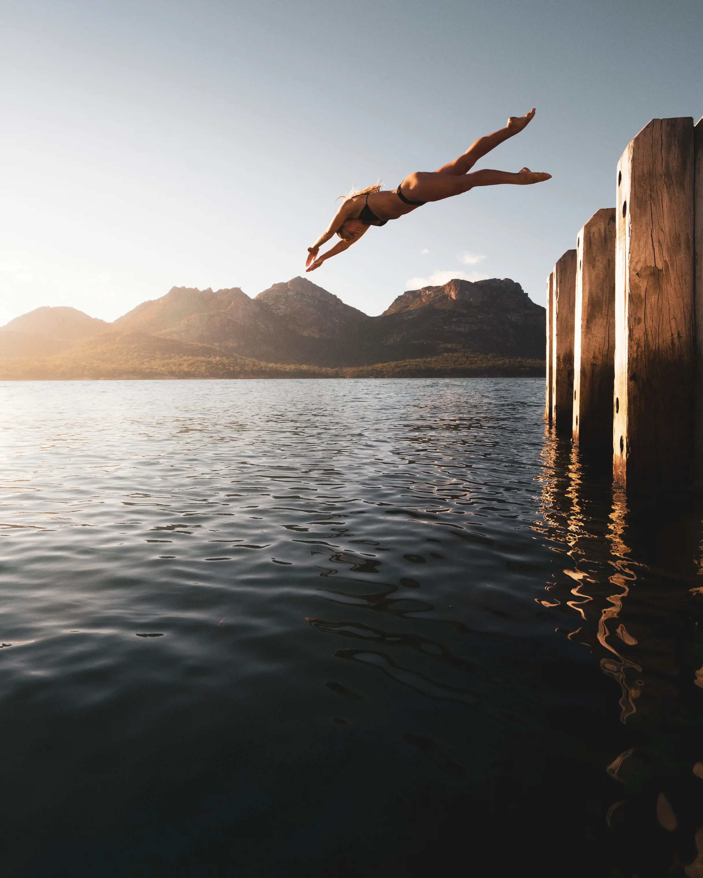 Female diving off Coles Bay Jetty, with mountains in the background, Coles Bay.