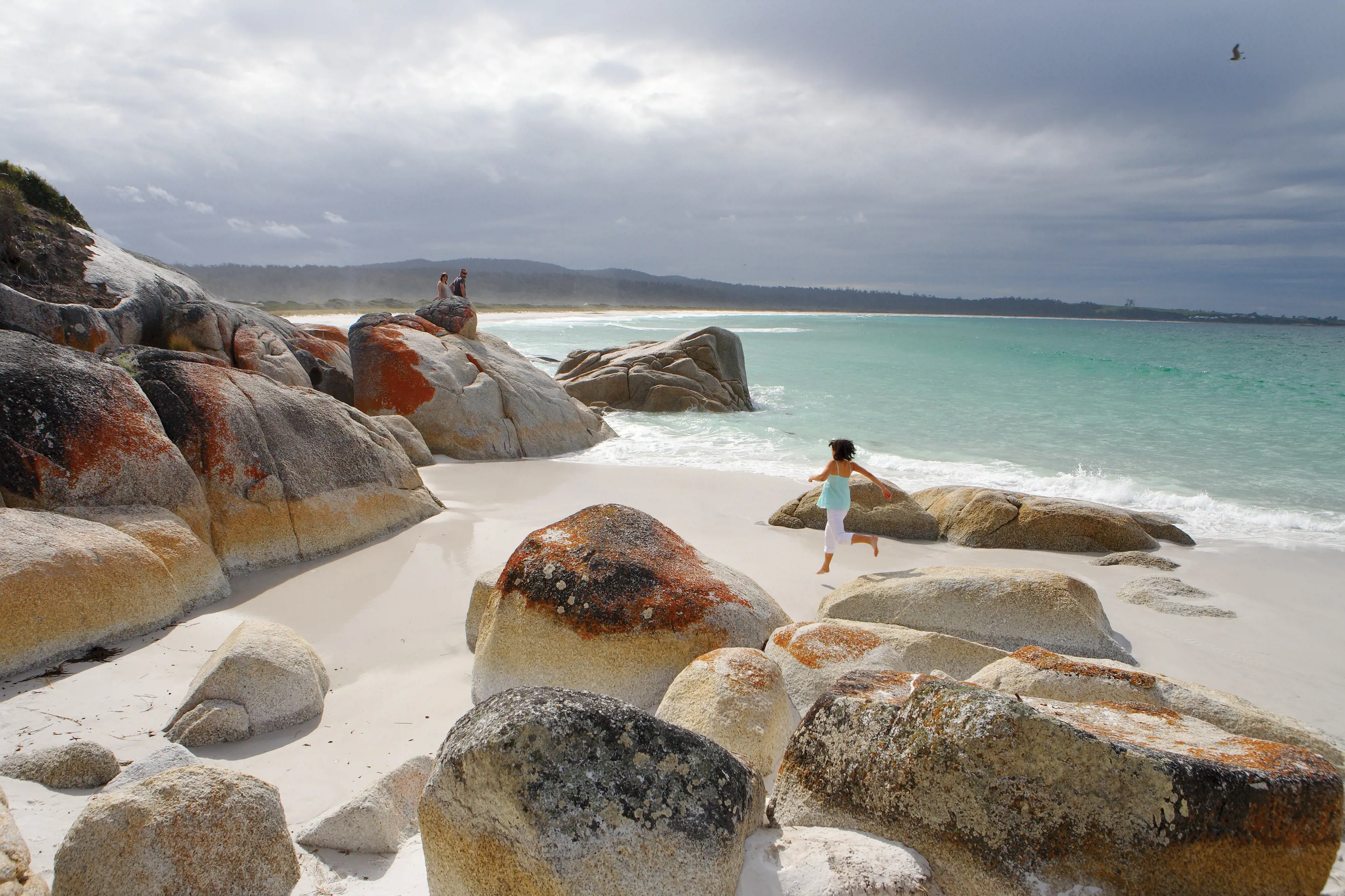 Woman running along Seaton Cove beach. Surrounded by rocks and the ocean.