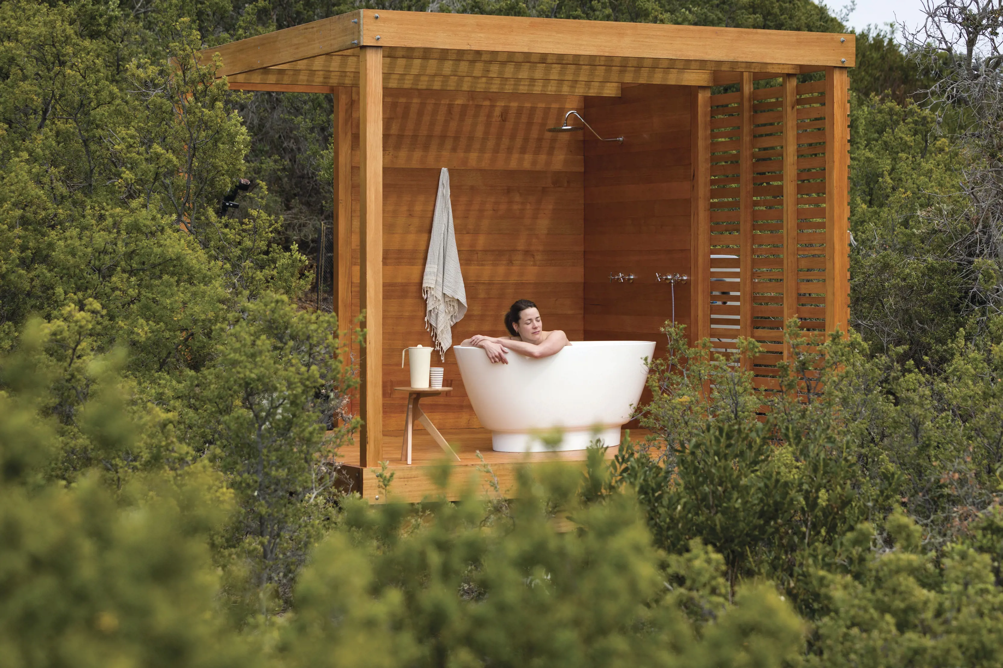A person relaxes in the outdoor spa, located in an idyllic setting adjacent to the iconic Bay of Fires Lodge.