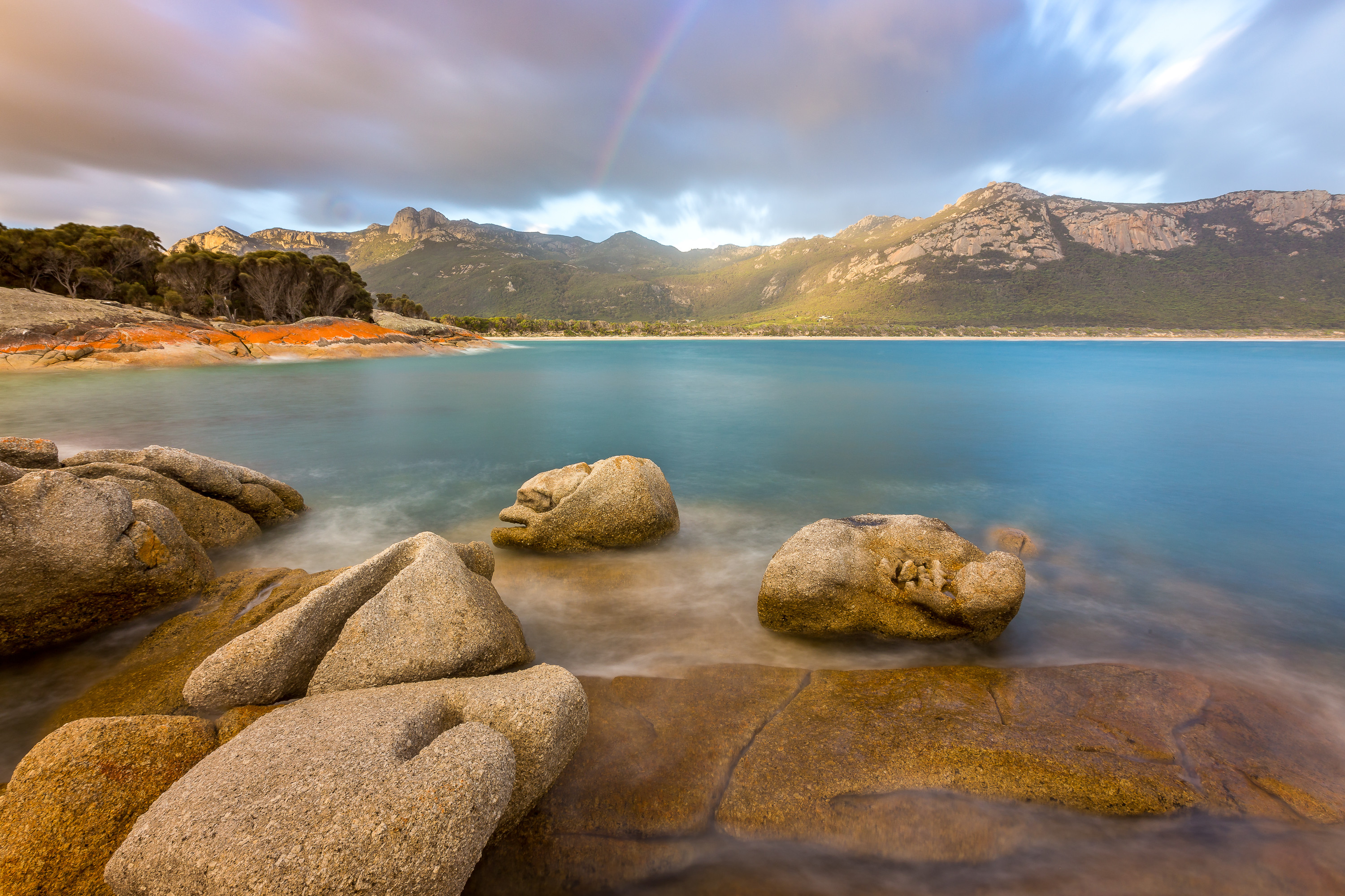 Breathtaking vibrant image of Trousers Point with a rainbow above a clear, calm ocean.