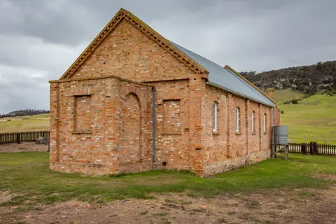 Image of the Wybalenna Chapel, built by brick. Surrounded by lush farmland.